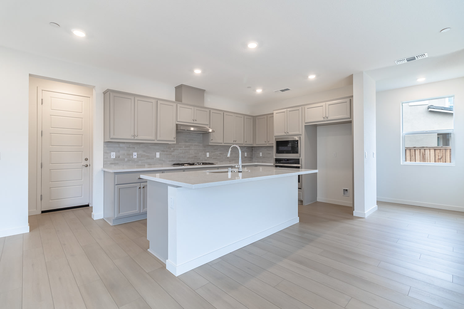 A modern, open-concept kitchen with white cabinets, a white island, and hardwood floors, set against a bright and airy background.