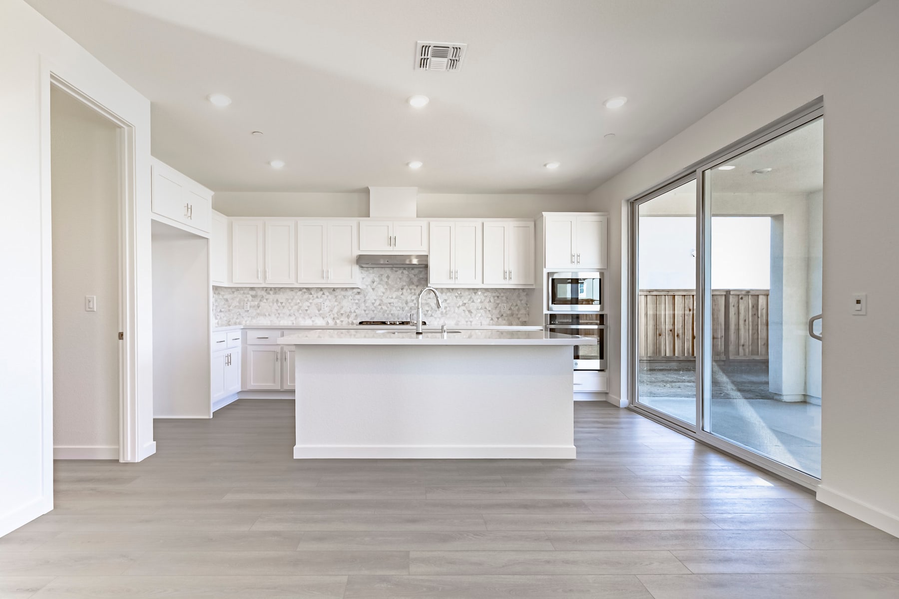A modern, open-concept kitchen with white cabinets, a central island, and hardwood floors leading to a sliding glass door that provides access to an outdoor area.