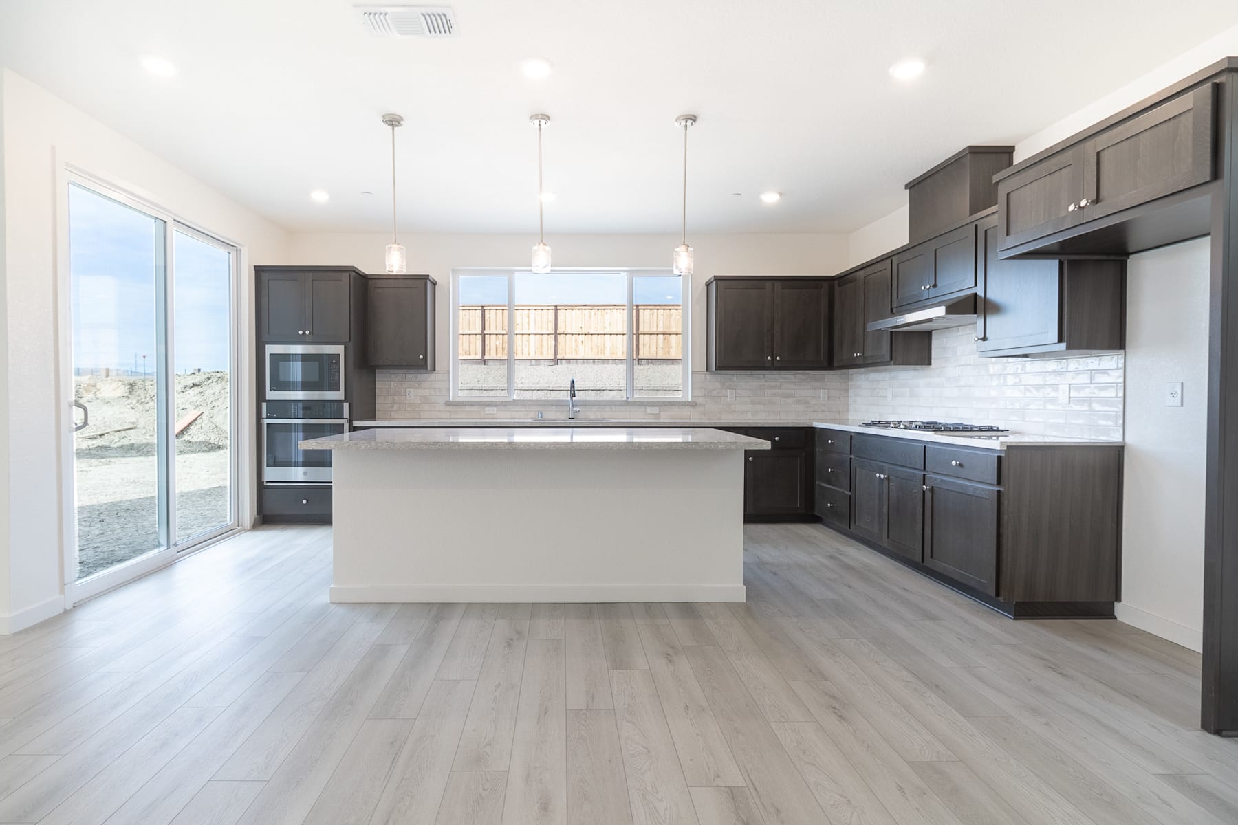 A modern, open-concept kitchen with dark cabinets, a white countertop, and a large window providing natural light.
