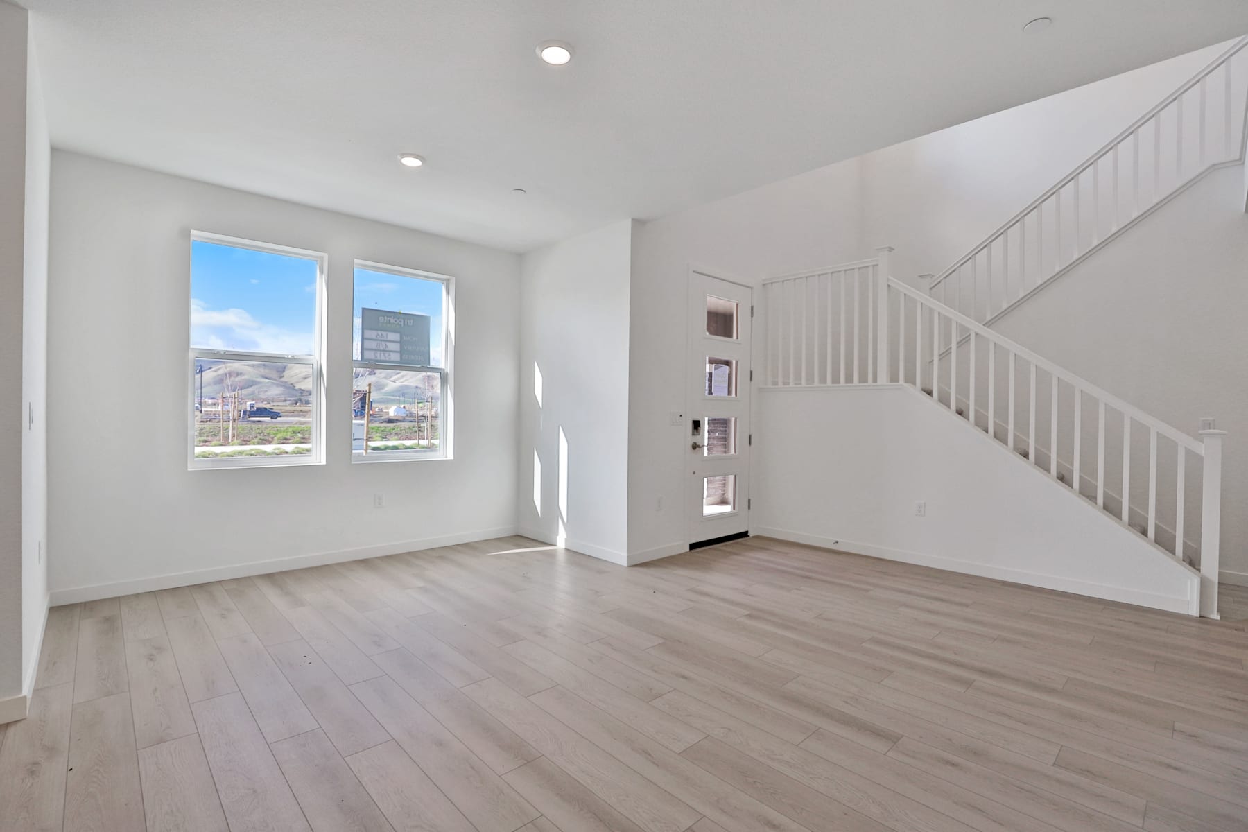 A bright and spacious interior with a staircase, hardwood floors, and large windows providing a view of the outdoors.