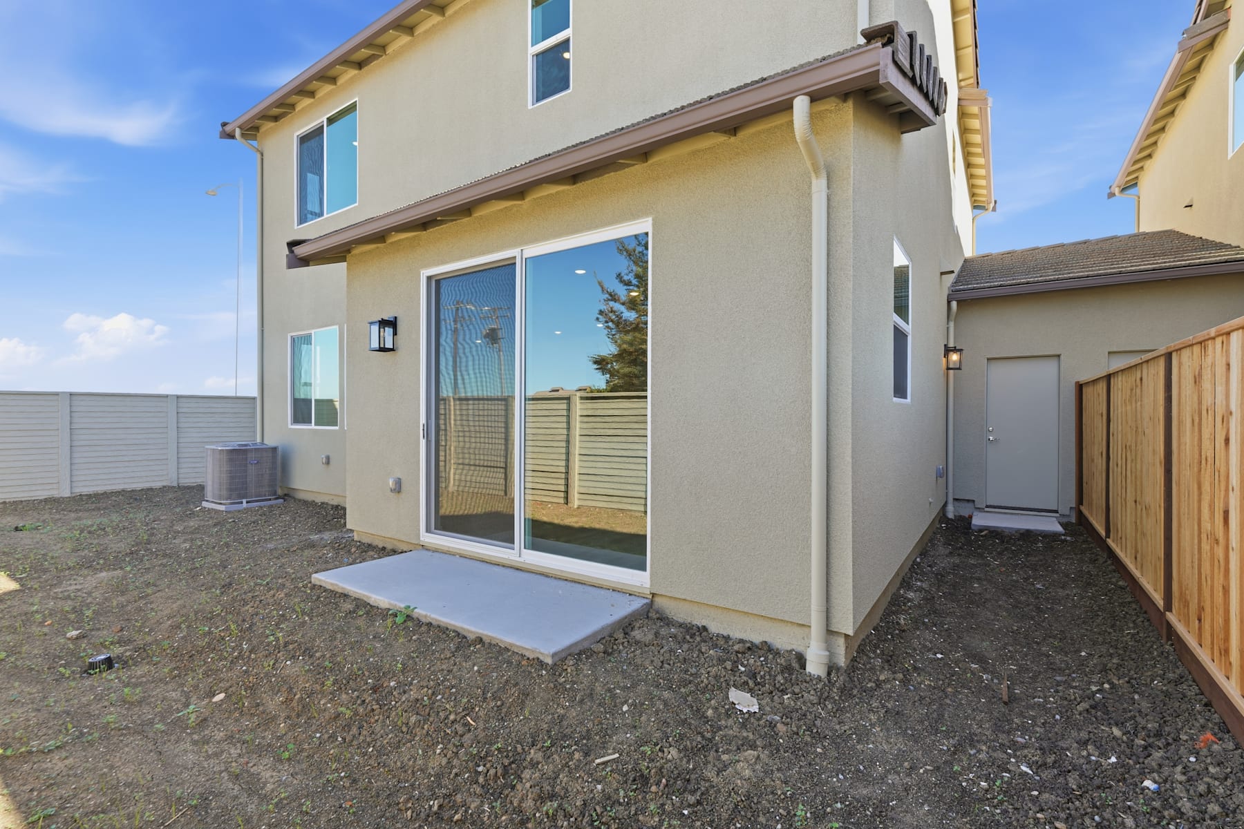 A modern two-story residential building with a patio and landscaping in the foreground, set against a clear blue sky.