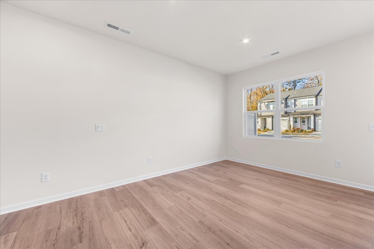A spacious, well-lit room with a large window, hardwood floors, and a minimalist design aesthetic.