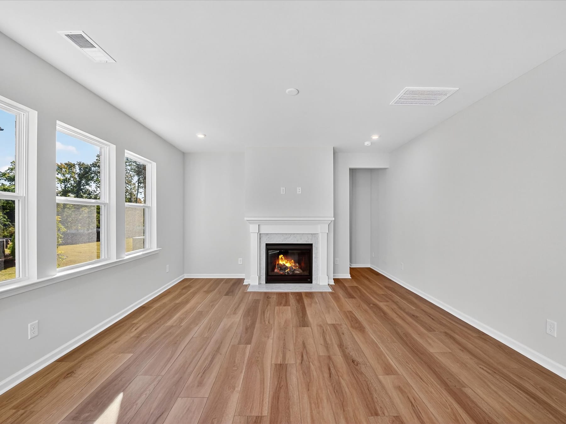 A spacious, well-lit room with a fireplace and large windows overlooking a scenic outdoor area, featuring hardwood floors and a minimalist, modern design.