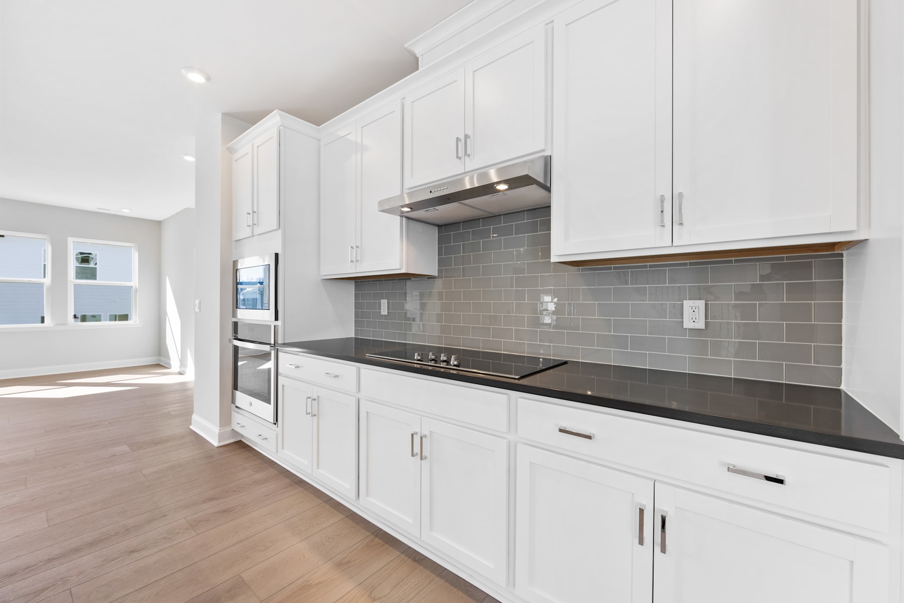 A modern, well-equipped kitchen with white cabinets, gray subway tile backsplash, and a sleek black countertop.