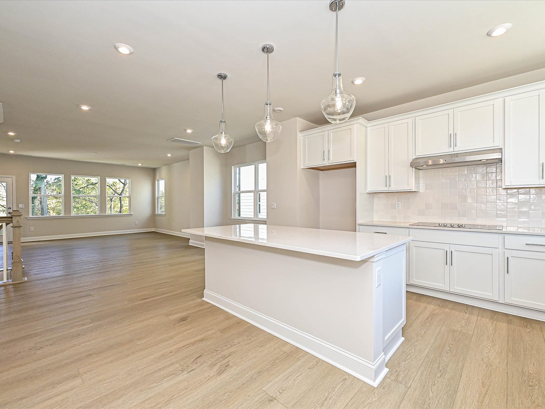 A spacious and modern kitchen with white cabinets, a large island, and hardwood floors, surrounded by large windows that let in natural light.
