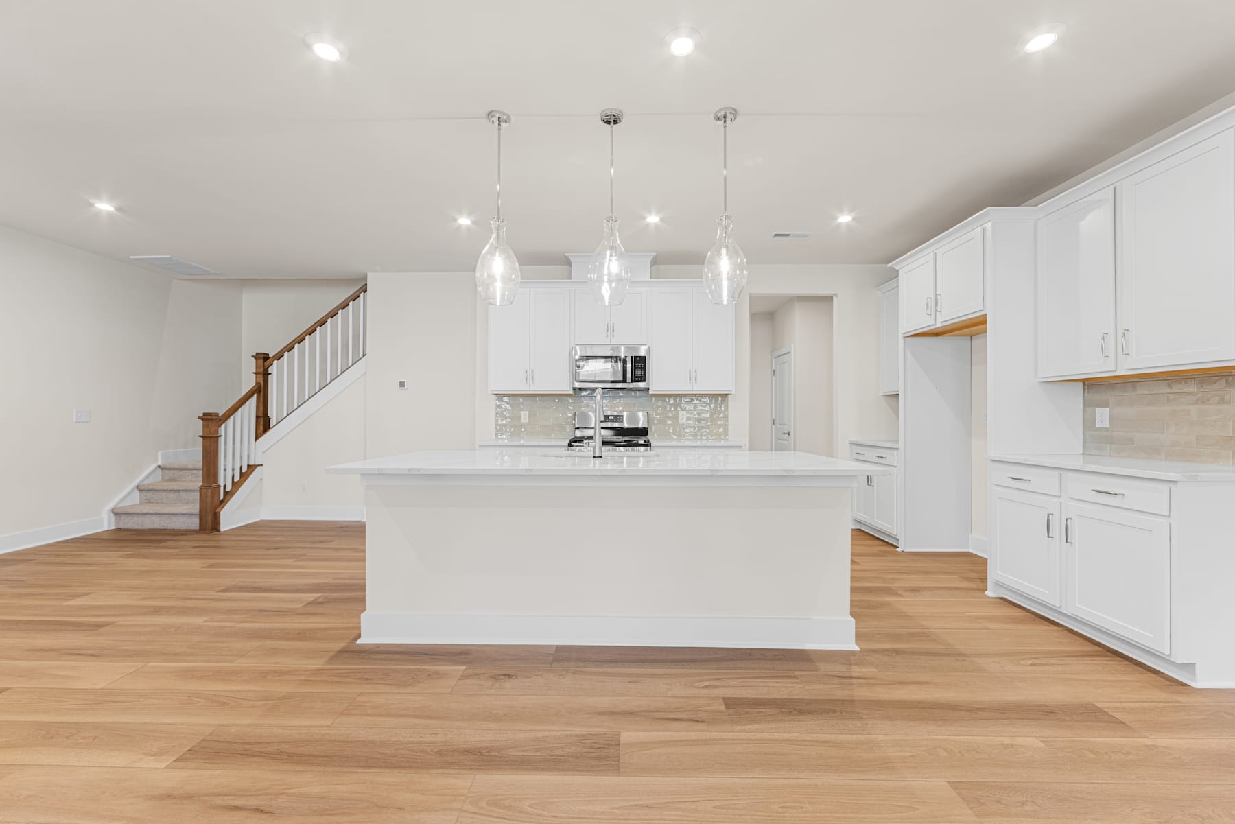 A modern, open-concept kitchen with white cabinets, a central island, and hardwood floors, illuminated by pendant lights.