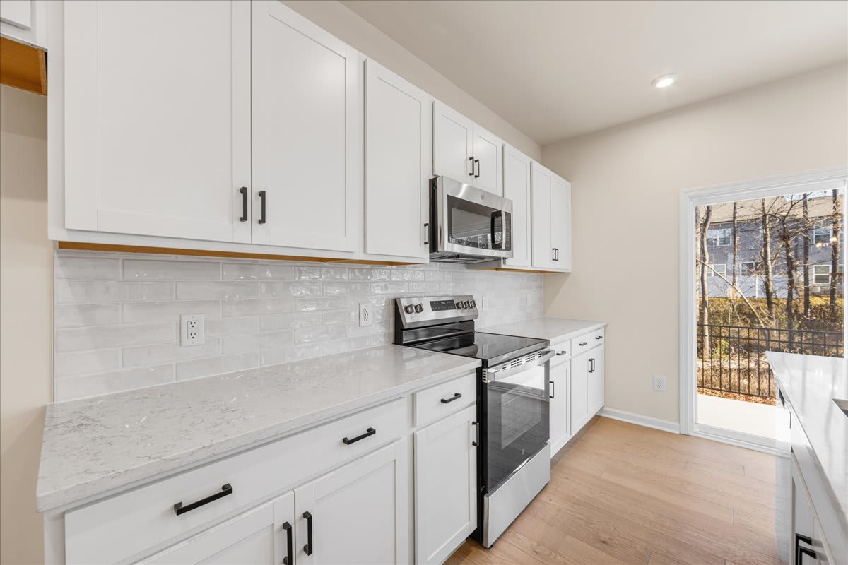 A modern, well-lit kitchen with white cabinets, stainless steel appliances, and a tiled backsplash, set against a backdrop of a window overlooking an outdoor scene.