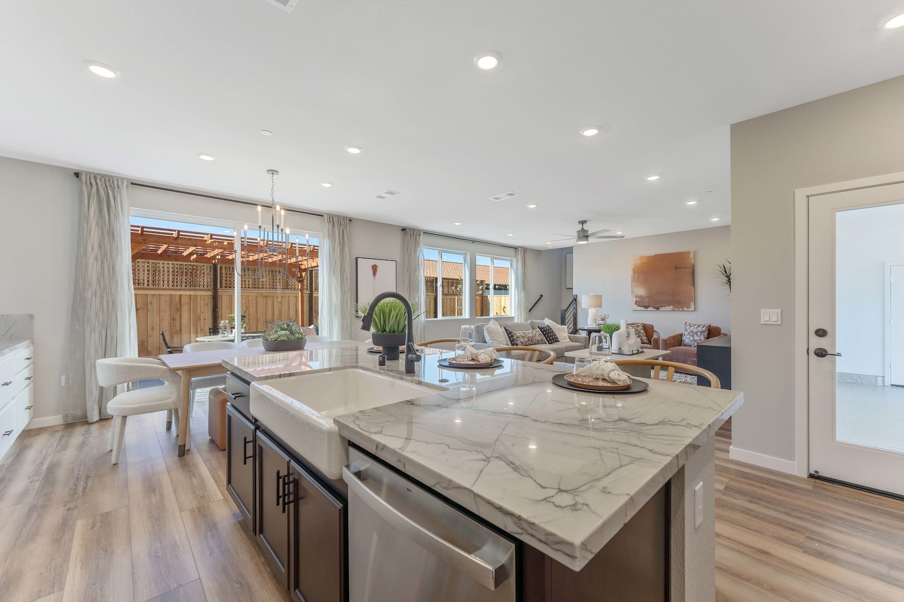 A modern and spacious kitchen with a large marble-topped island, open-concept living area, and natural light streaming in through the windows.
