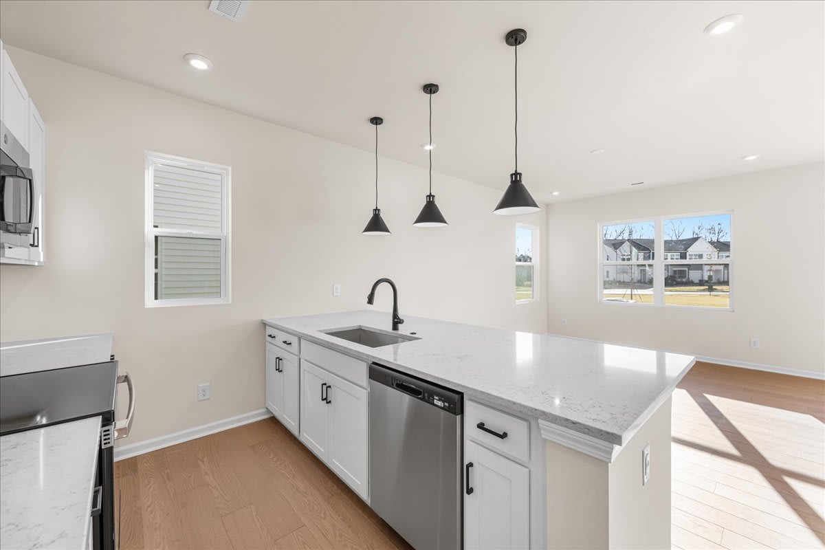 A modern, well-lit kitchen with white cabinets, stainless steel appliances, and pendant lights hanging above a central island.