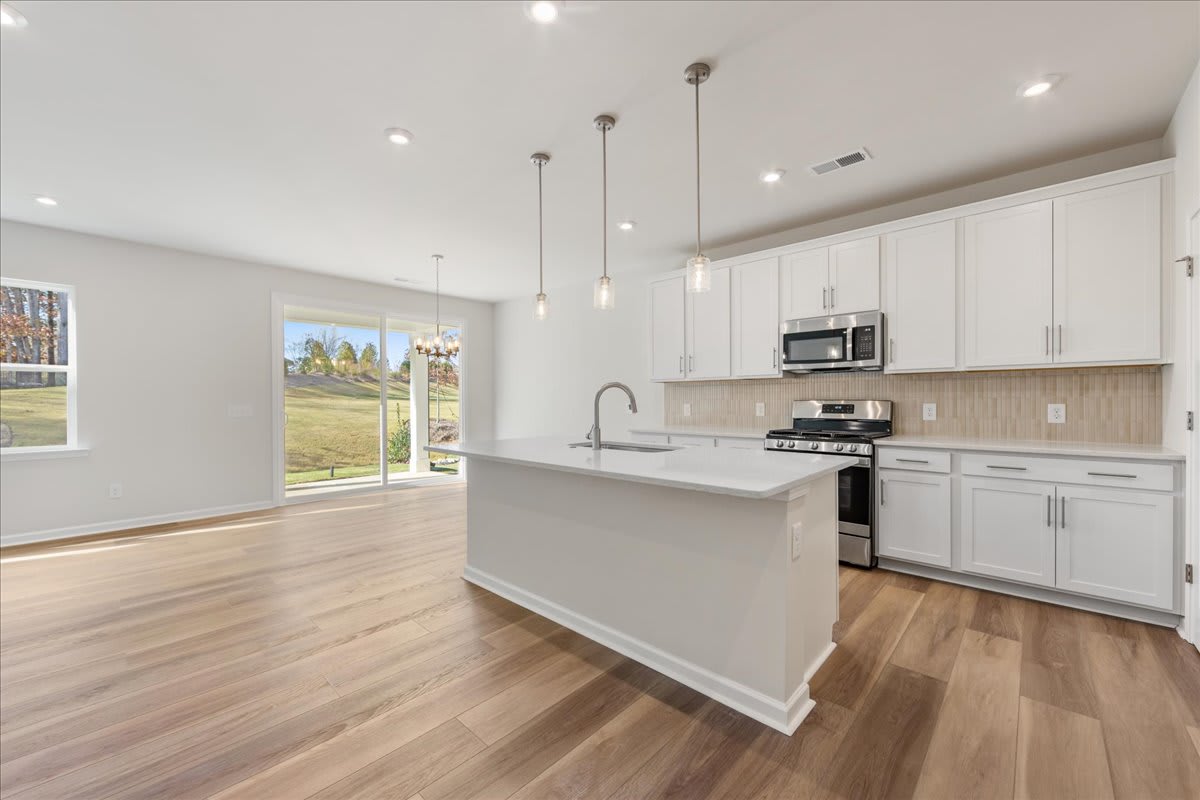 A modern, open-concept kitchen with white cabinets, stainless steel appliances, and a large window overlooking a scenic outdoor landscape.