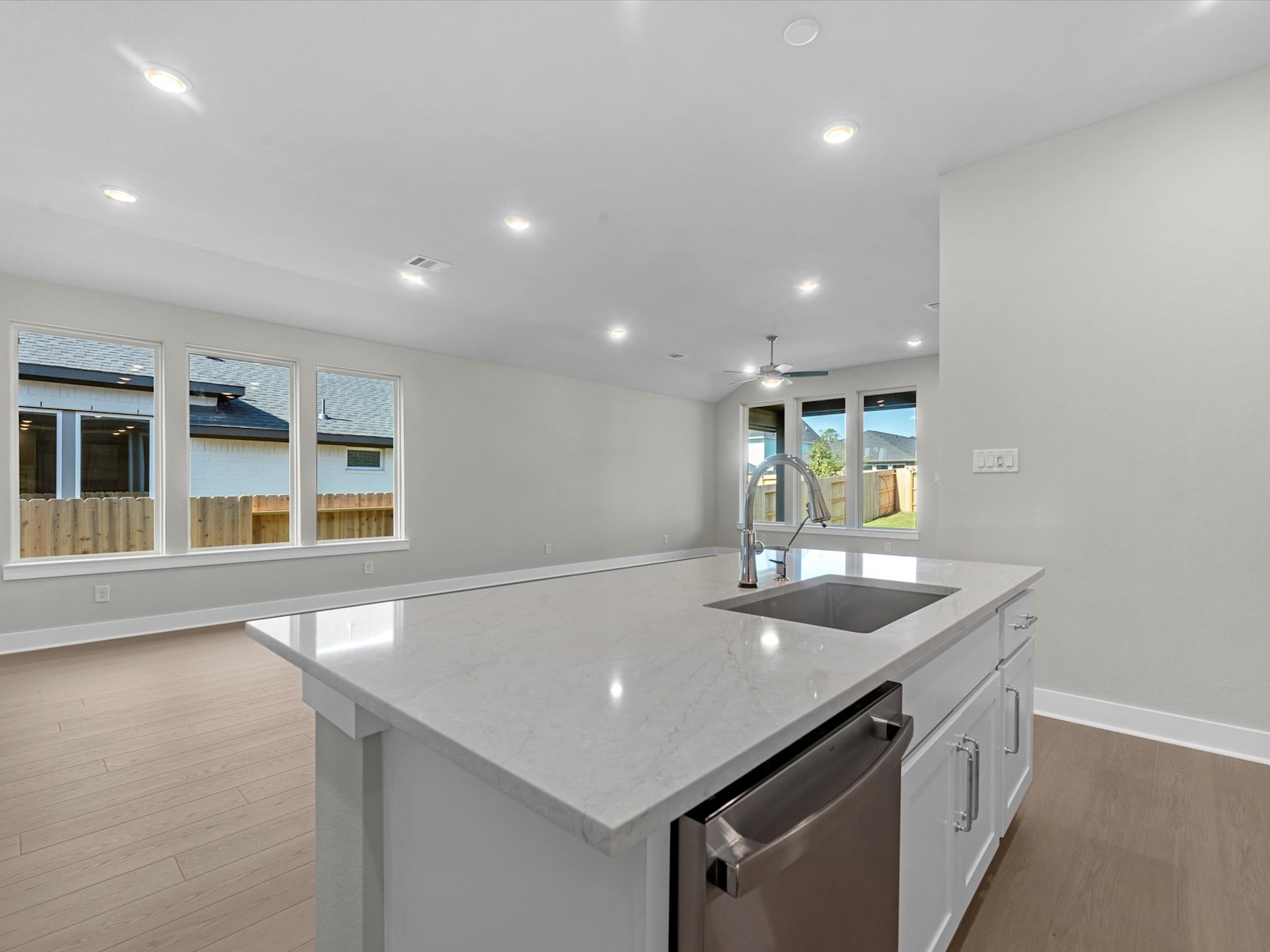 A modern, open-concept kitchen with a large, white quartz countertop, stainless steel appliances, and recessed lighting illuminating the space.