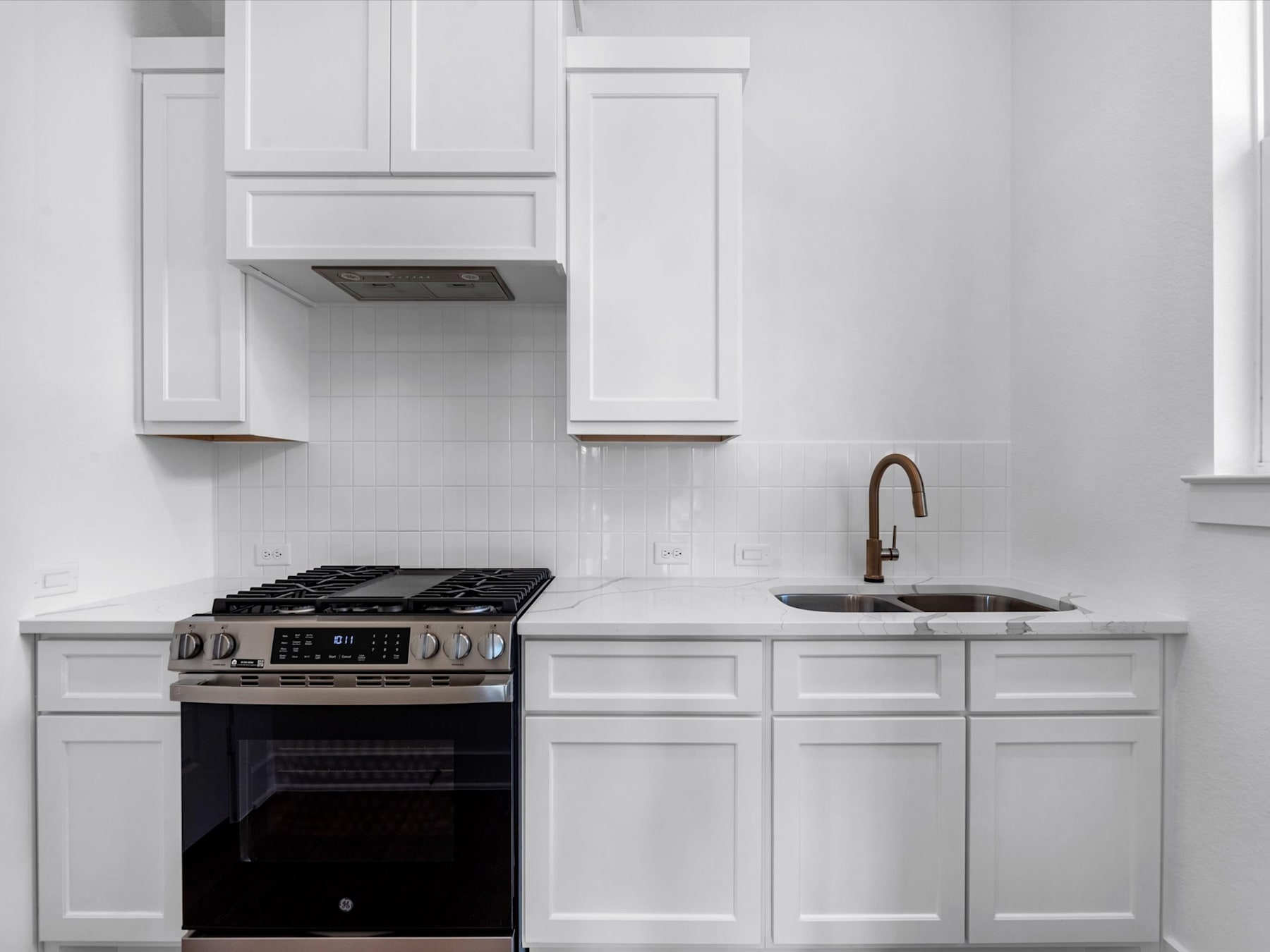 A modern, white kitchen with a gas stove, sink, and cabinets, set against a bright and clean background.