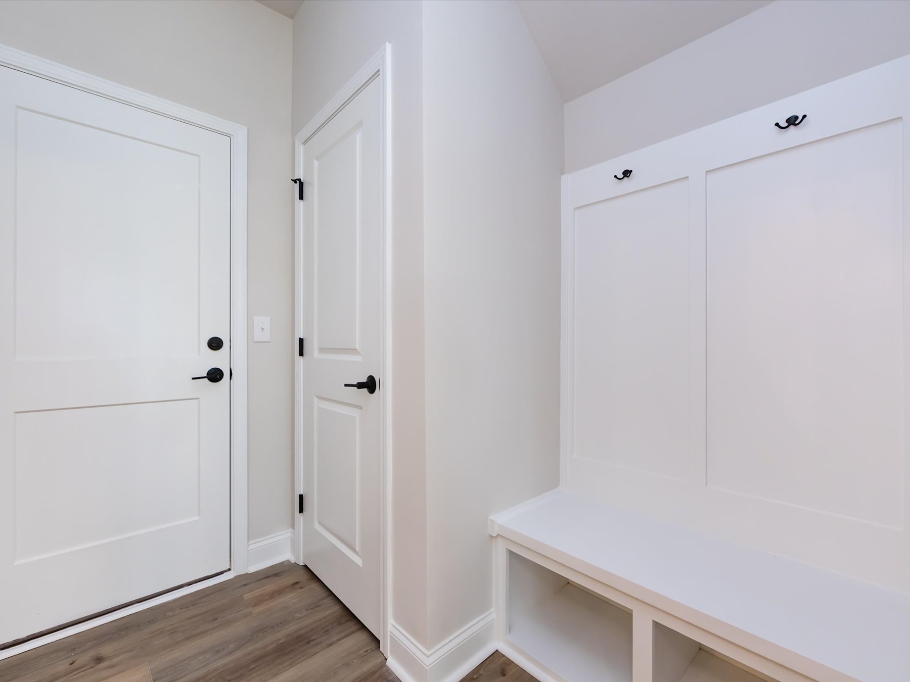 A bright, minimalist entryway with a white door, built-in storage, and a wooden floor.
