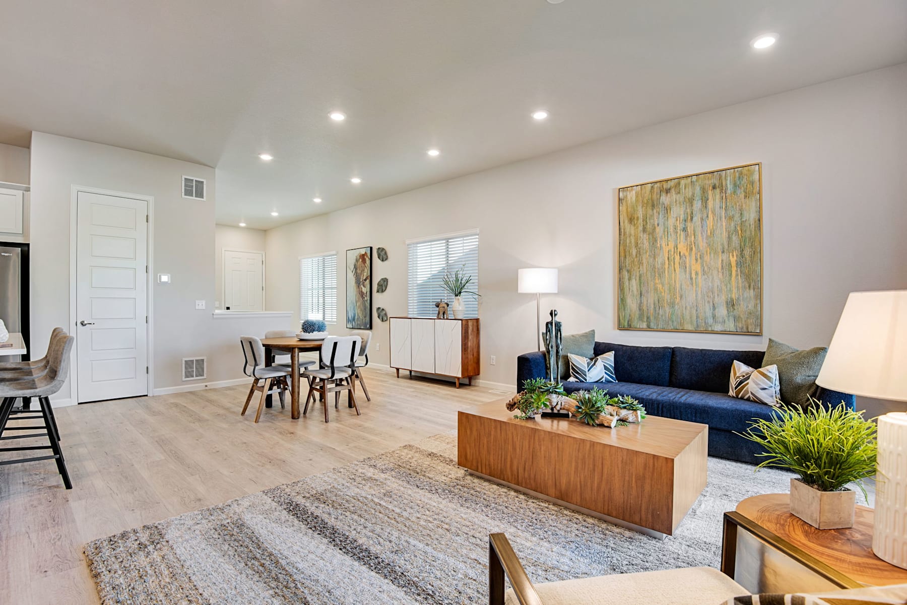 A modern and open-concept living space with a dining area, a navy blue sofa, and a wooden entertainment unit, complemented by vibrant artwork and potted plants.