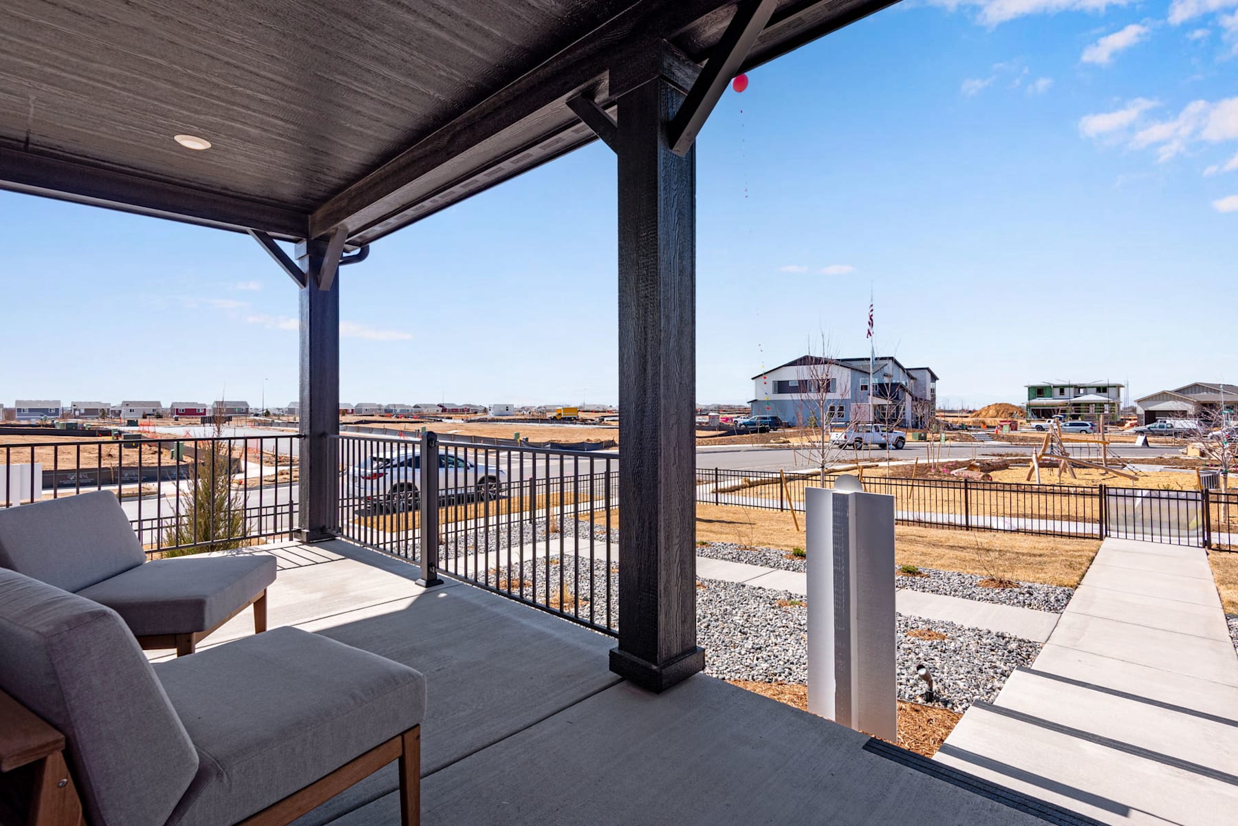 The image shows a covered patio or balcony overlooking a construction site in the background, with a clear blue sky and scattered clouds visible.