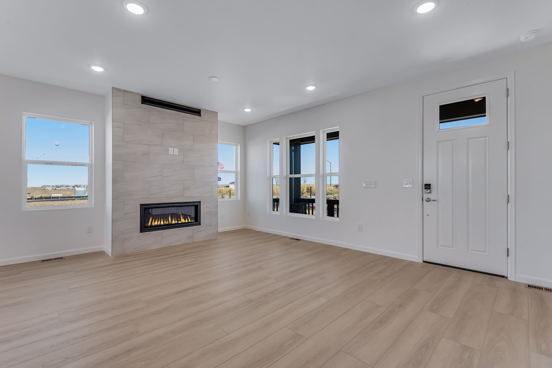 A modern, minimalist living room with a fireplace, hardwood floors, and large windows providing natural light.