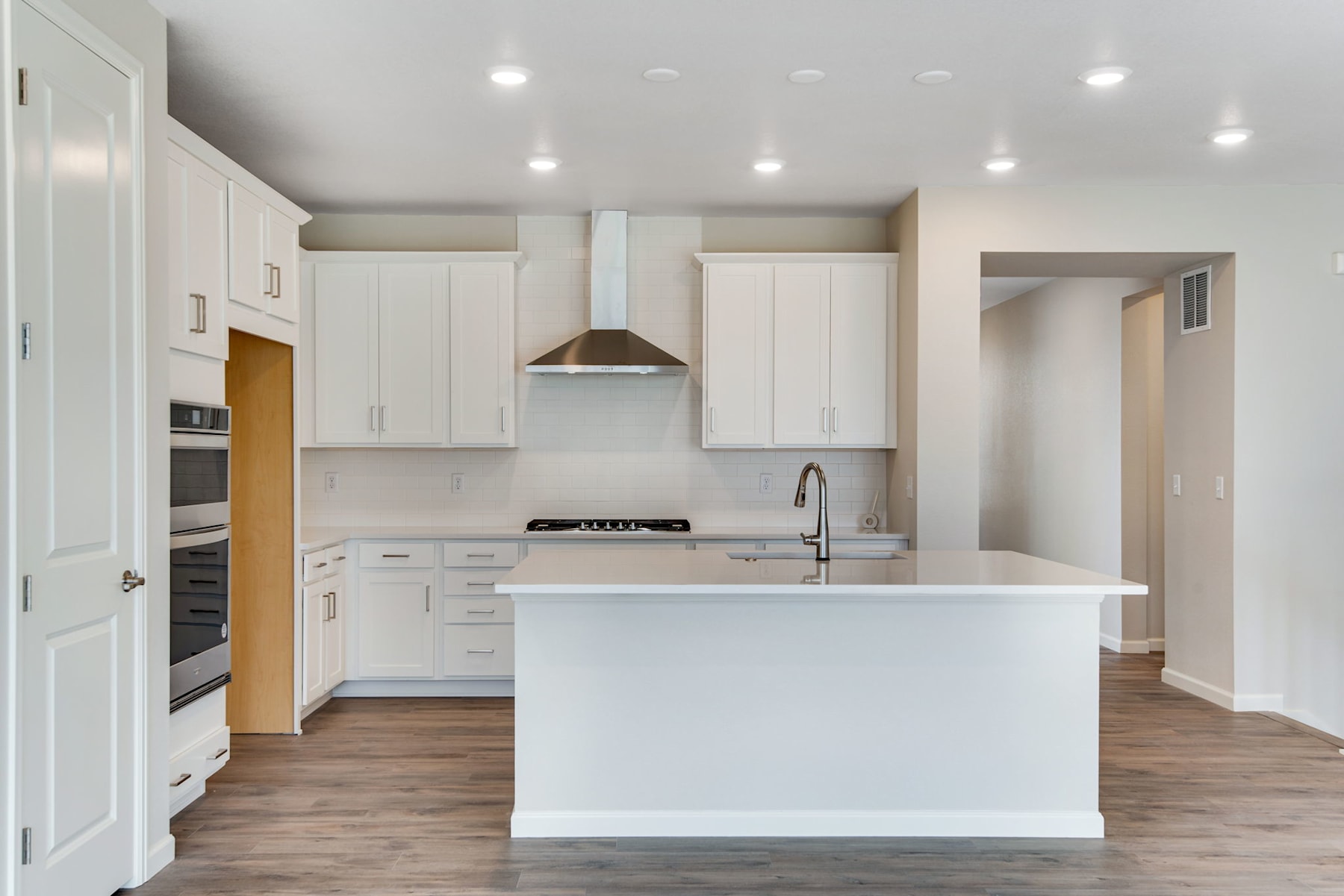 A modern, bright kitchen with white cabinets, a central island, and hardwood flooring.