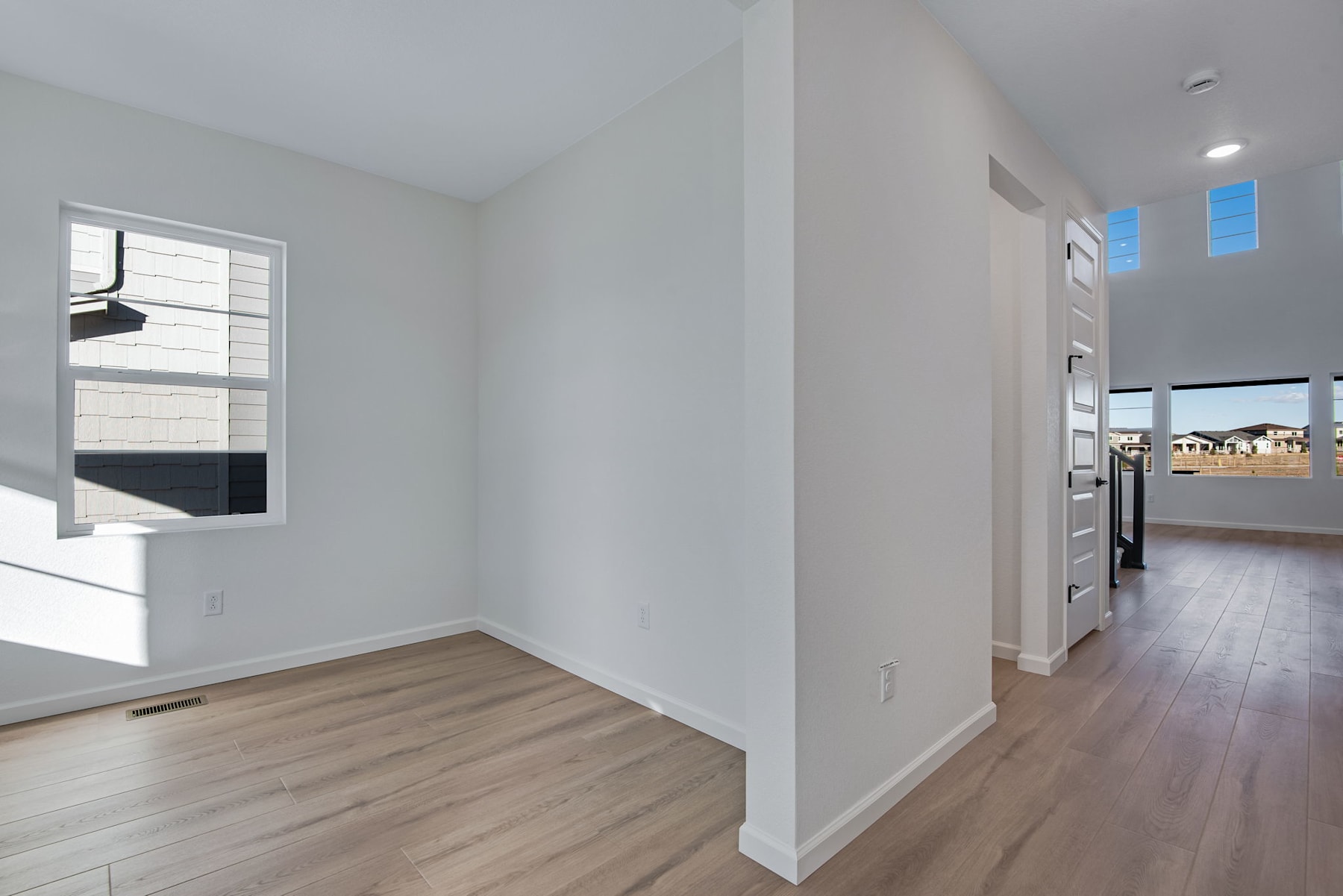 A spacious, well-lit room with white walls, hardwood floors, and a window providing natural light.