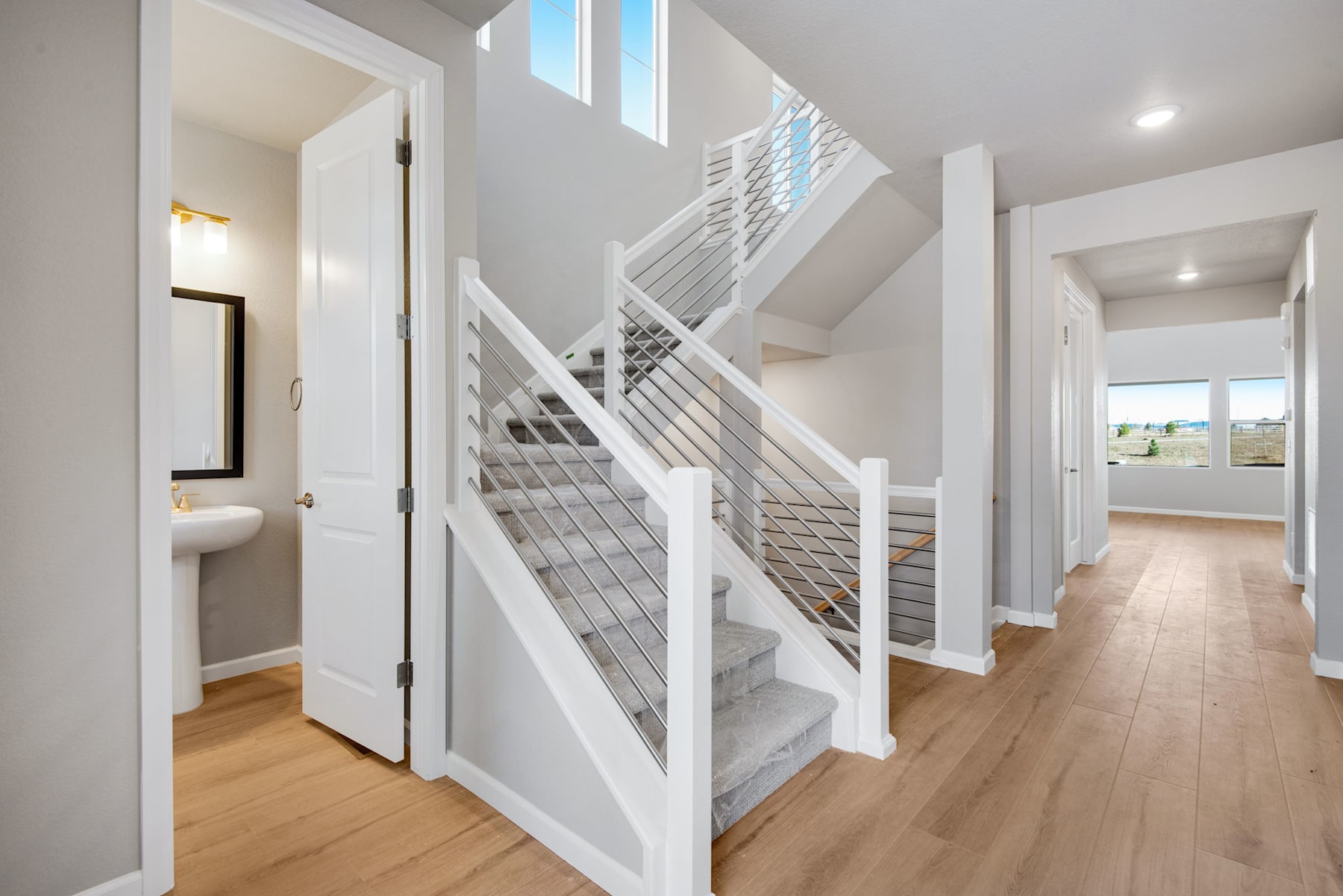 A bright and airy interior with a modern staircase, hardwood floors, and a hallway leading to other rooms.