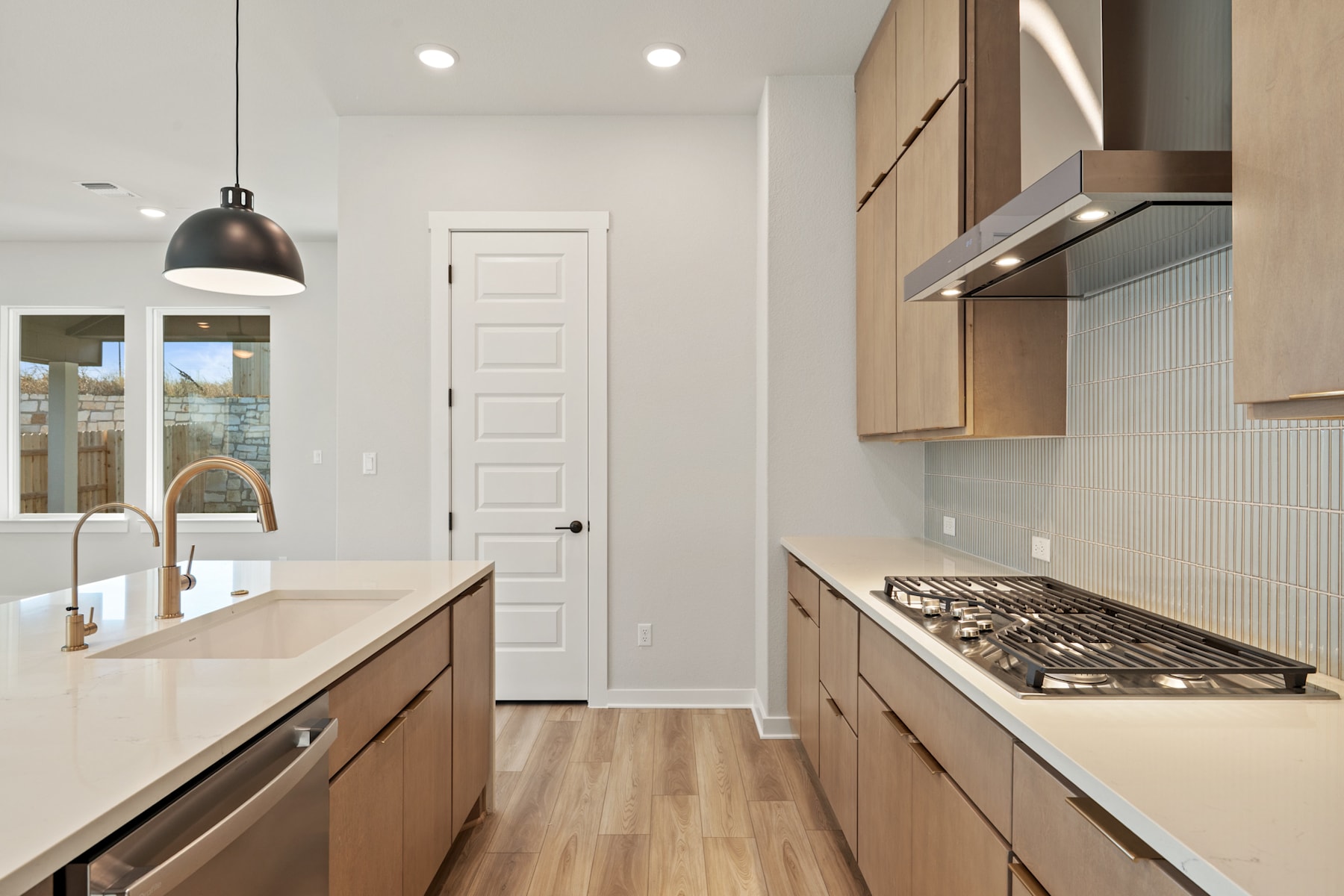 A modern and minimalist kitchen with light-colored cabinets, a gas stove, and a sink, set against a backdrop of a white door and walls.