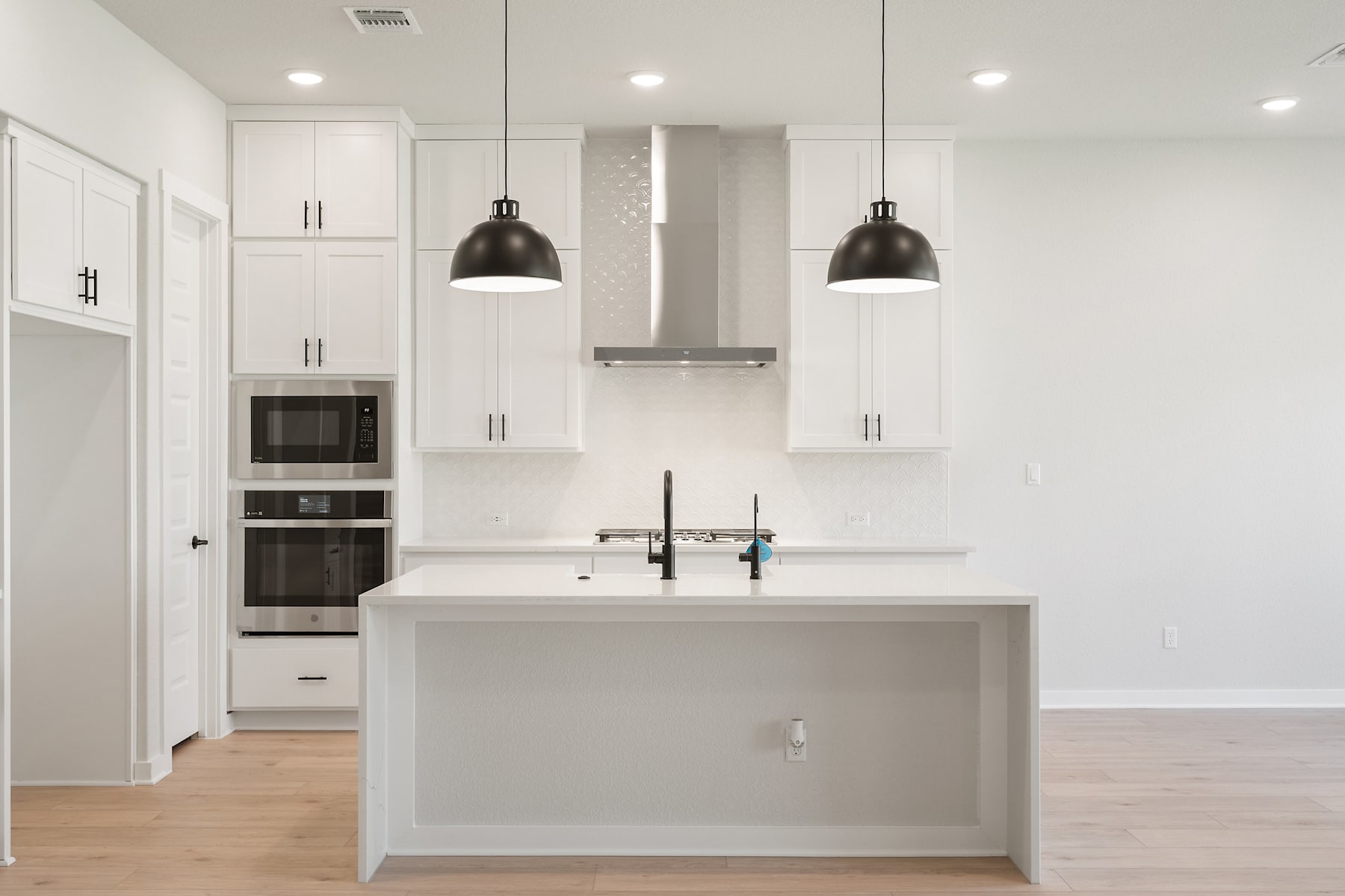 A modern, minimalist kitchen with white cabinets, a central island, and two black pendant lights hanging above.