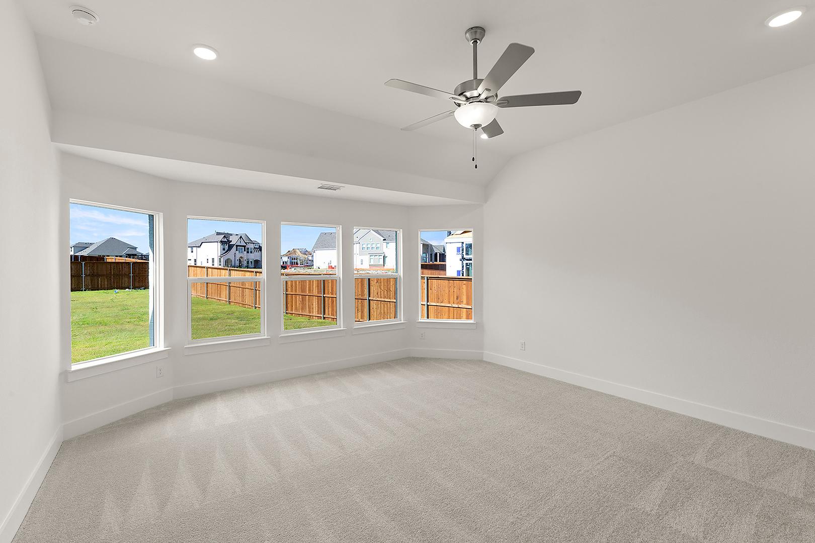 A spacious, well-lit room with a ceiling fan and large windows overlooking a fenced backyard.