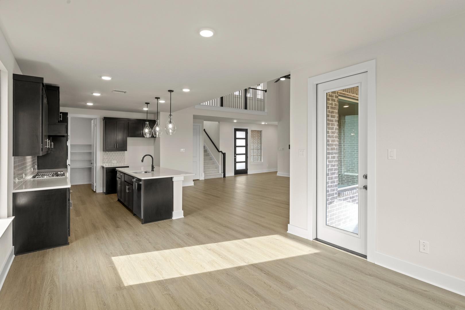A modern, open-concept kitchen and living space with sleek black appliances, light-colored hardwood floors, and a glass door leading to an exterior space.