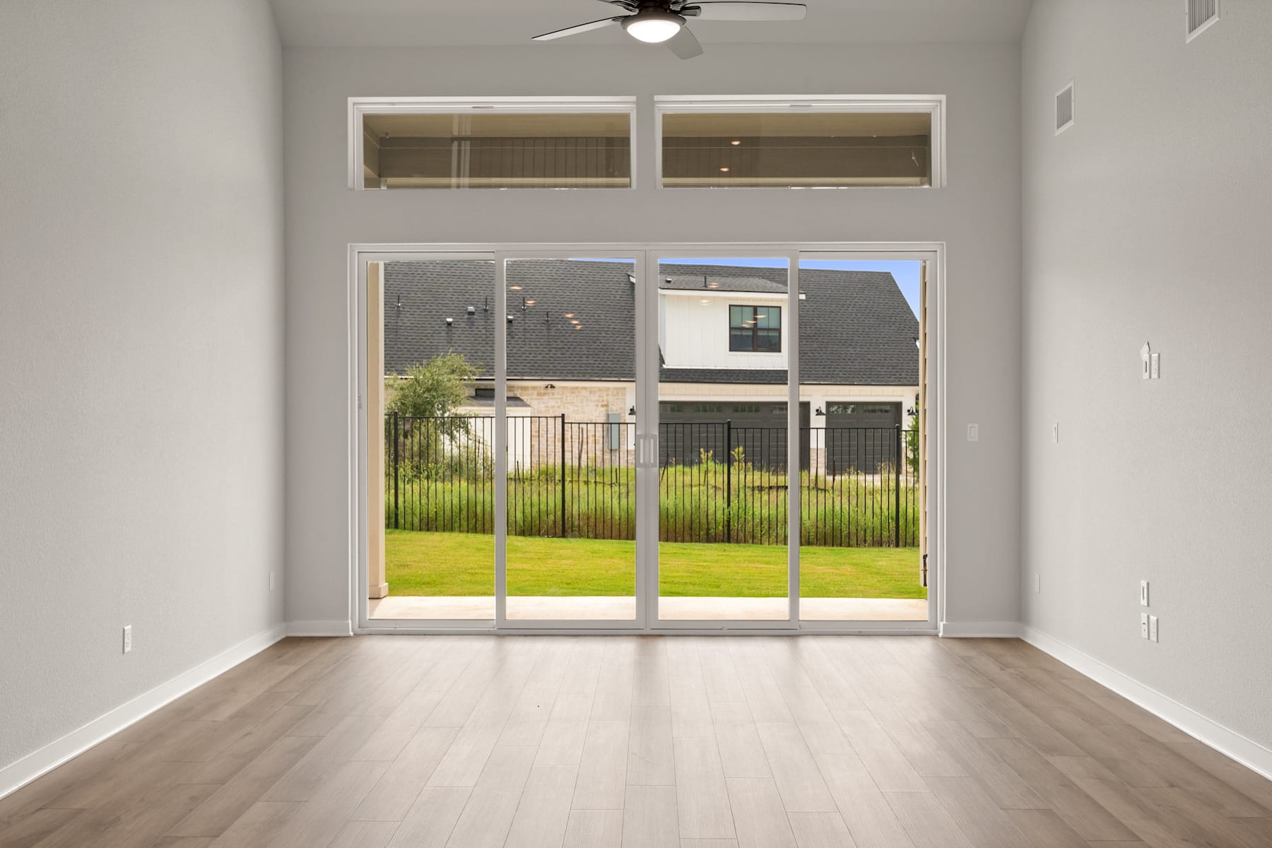 A spacious, well-lit room with a sliding glass door leading to a grassy outdoor area, featuring a ceiling fan and hardwood flooring.