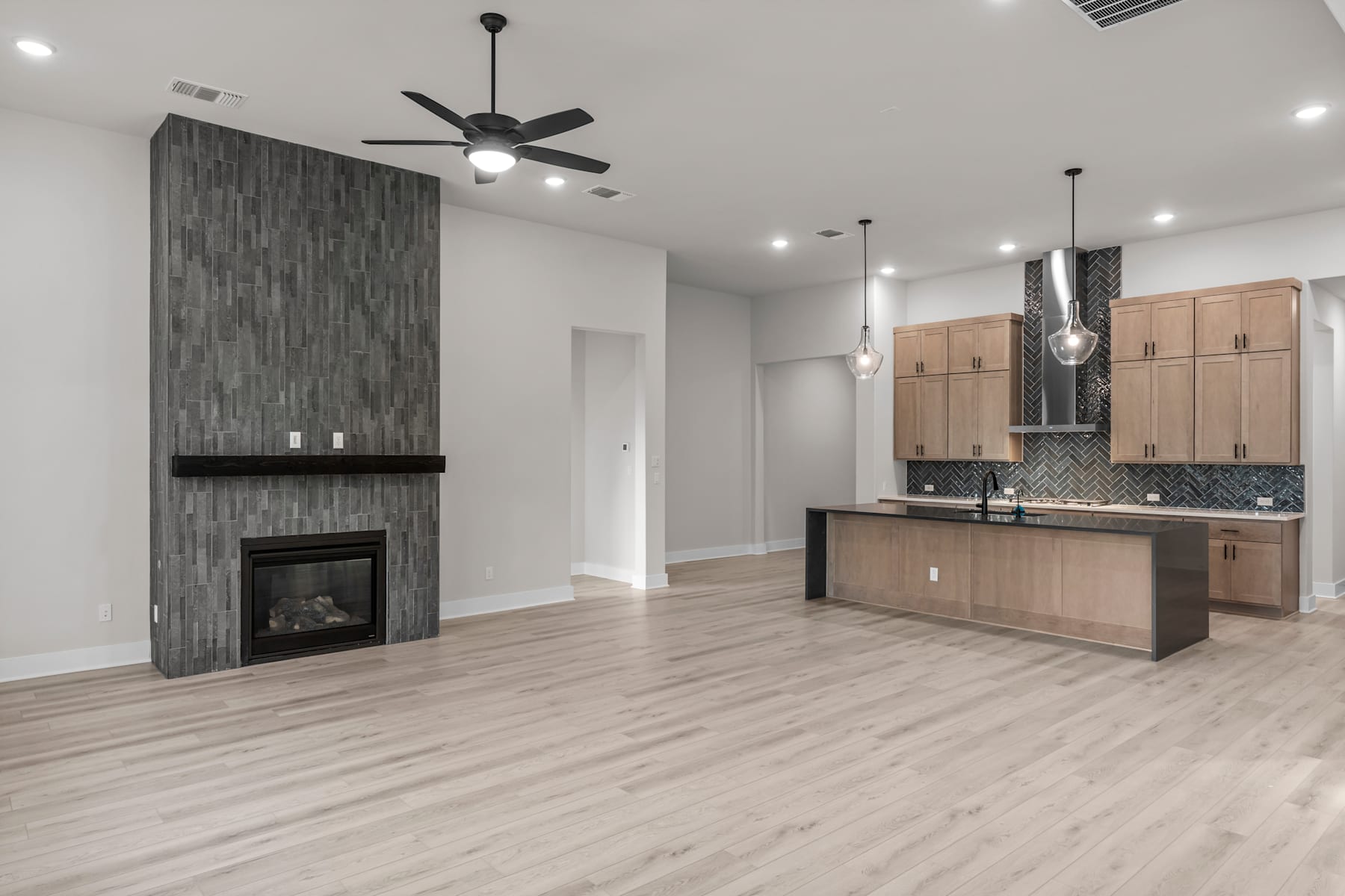 A modern, open-concept living space with a fireplace, wooden cabinets, and hardwood flooring.