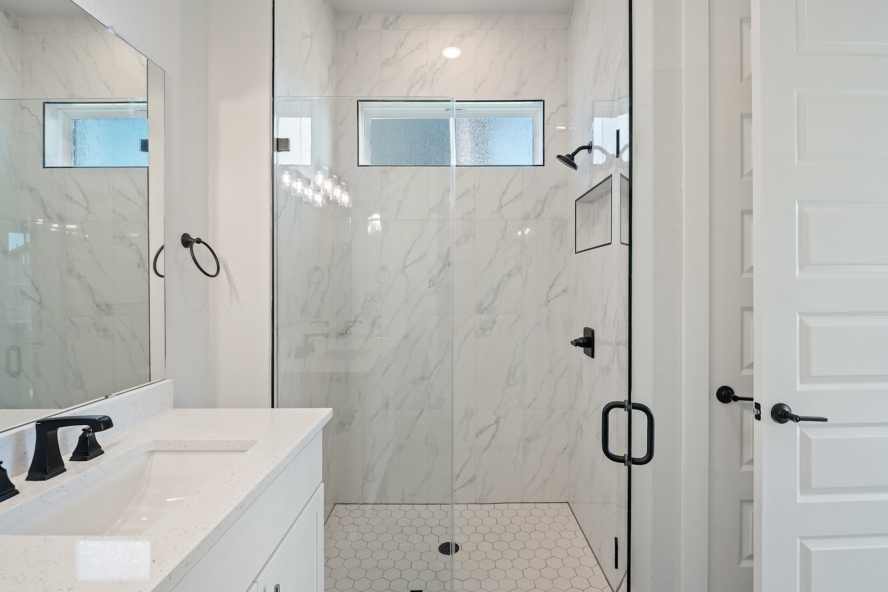A modern, minimalist bathroom with a large, glass-enclosed shower, a white vanity, and a tiled floor.