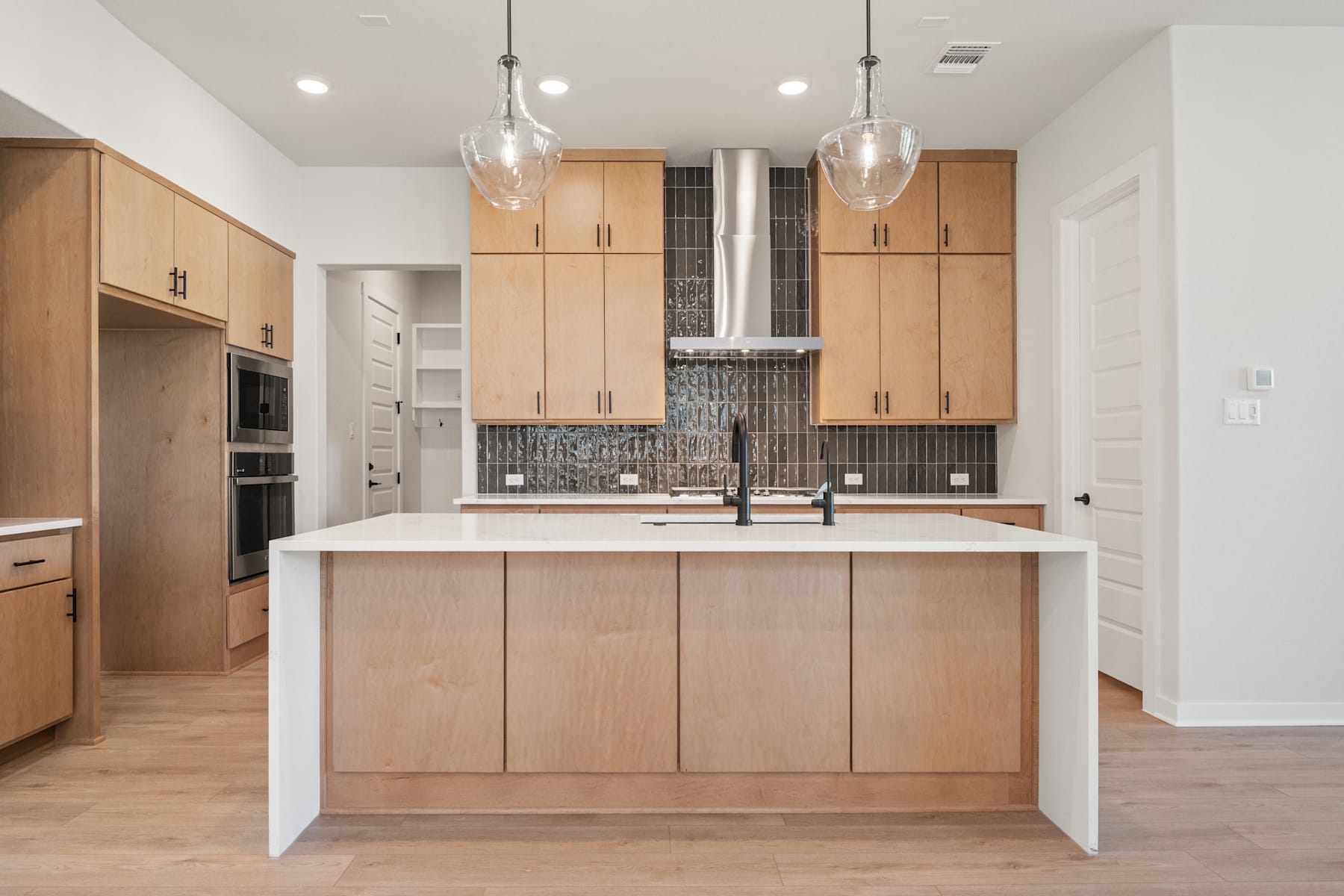 A modern, open-concept kitchen with light wood cabinetry, a white countertop, and pendant lighting fixtures.