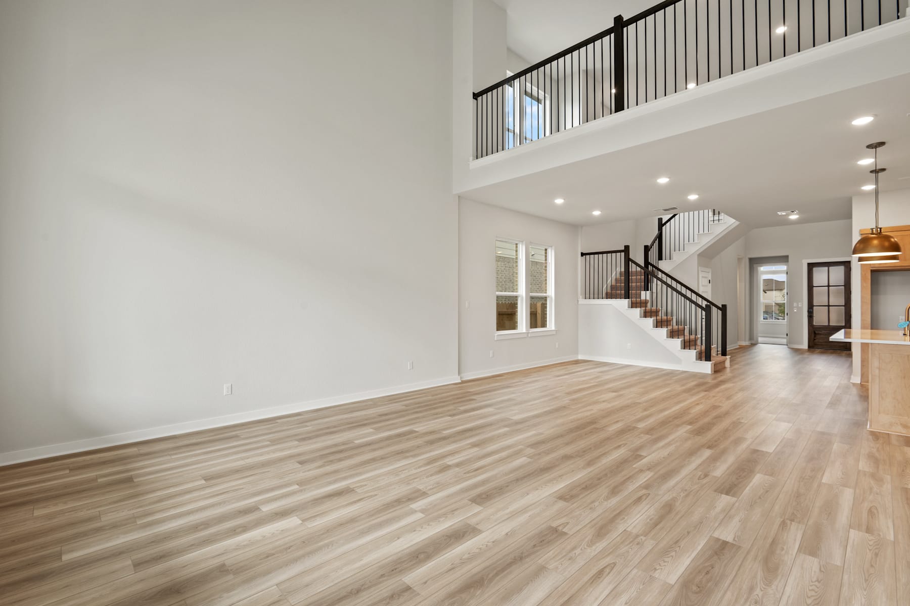A spacious and bright interior with a wooden floor, a staircase with a metal railing, and recessed lighting in the ceiling.