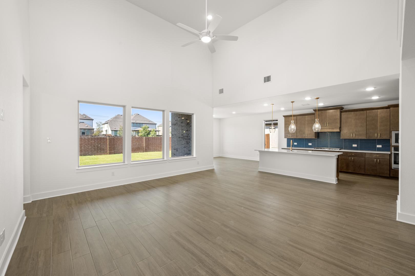 A spacious, open-concept living area with hardwood floors, large windows, and a modern kitchen visible in the background.