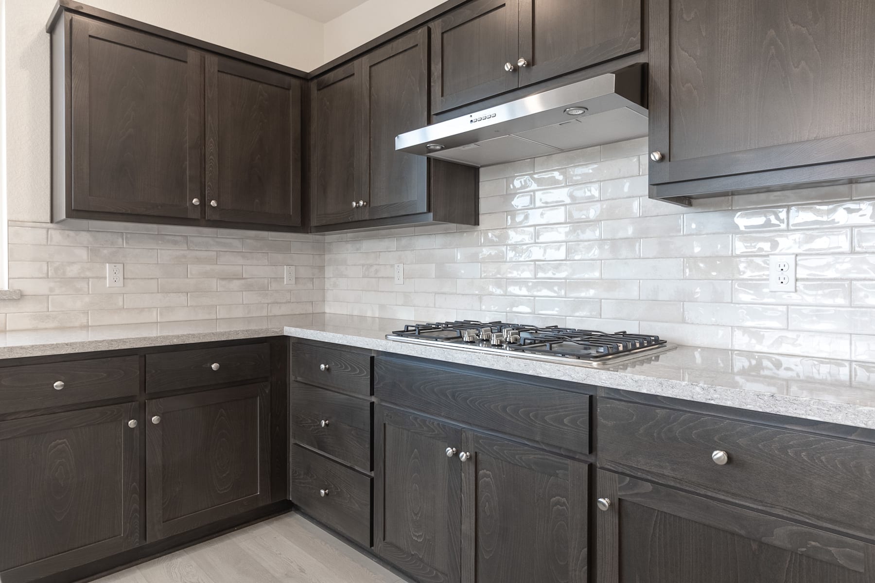 A modern kitchen with dark gray cabinets, a white subway tile backsplash, and a gas stove top.