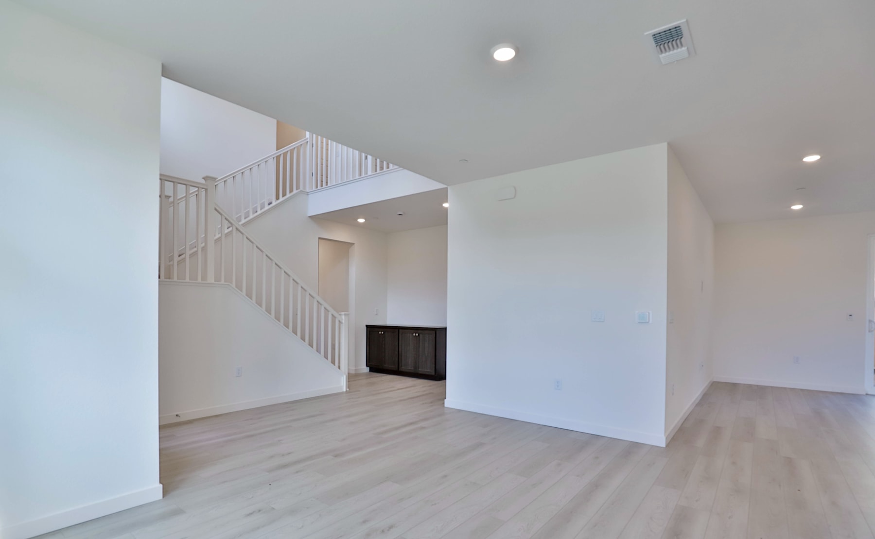 A spacious, minimalist interior with white walls, wooden floors, and a staircase leading to an upper level.