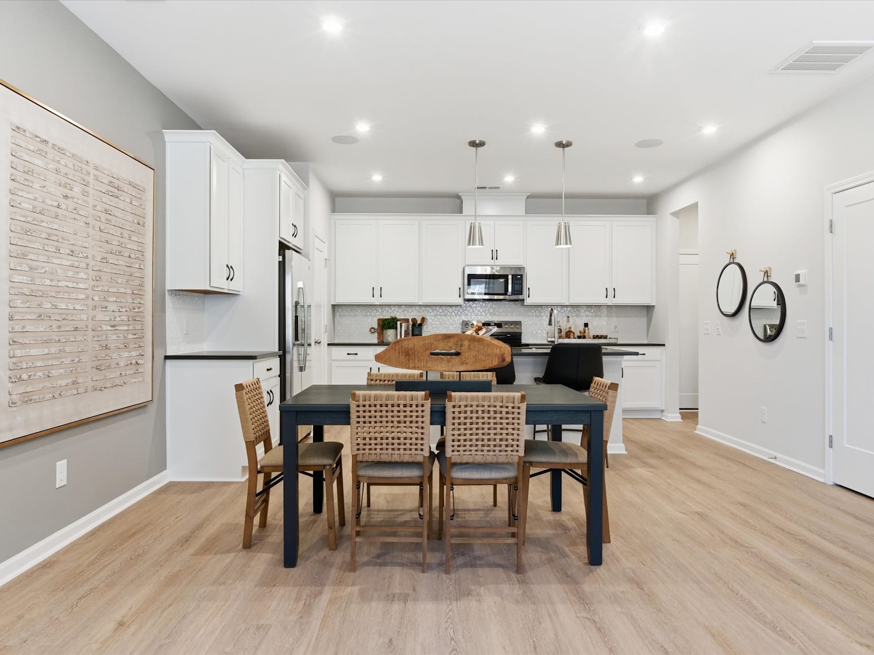 A modern, open-concept kitchen and dining area with white cabinets, stainless steel appliances, and a wooden dining table with wicker chairs.
