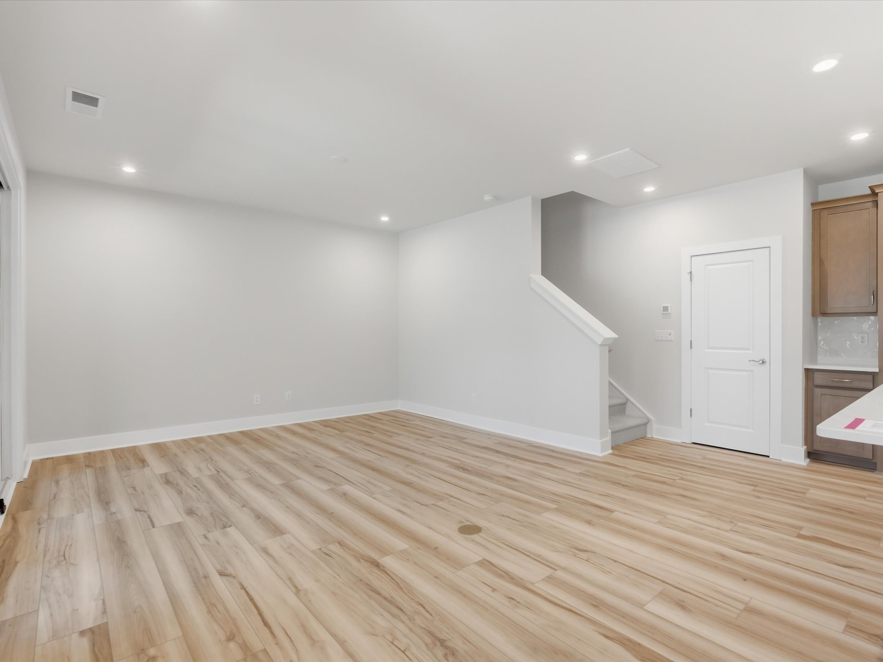 An empty room with white walls, a wooden floor, and a doorway leading to another area.