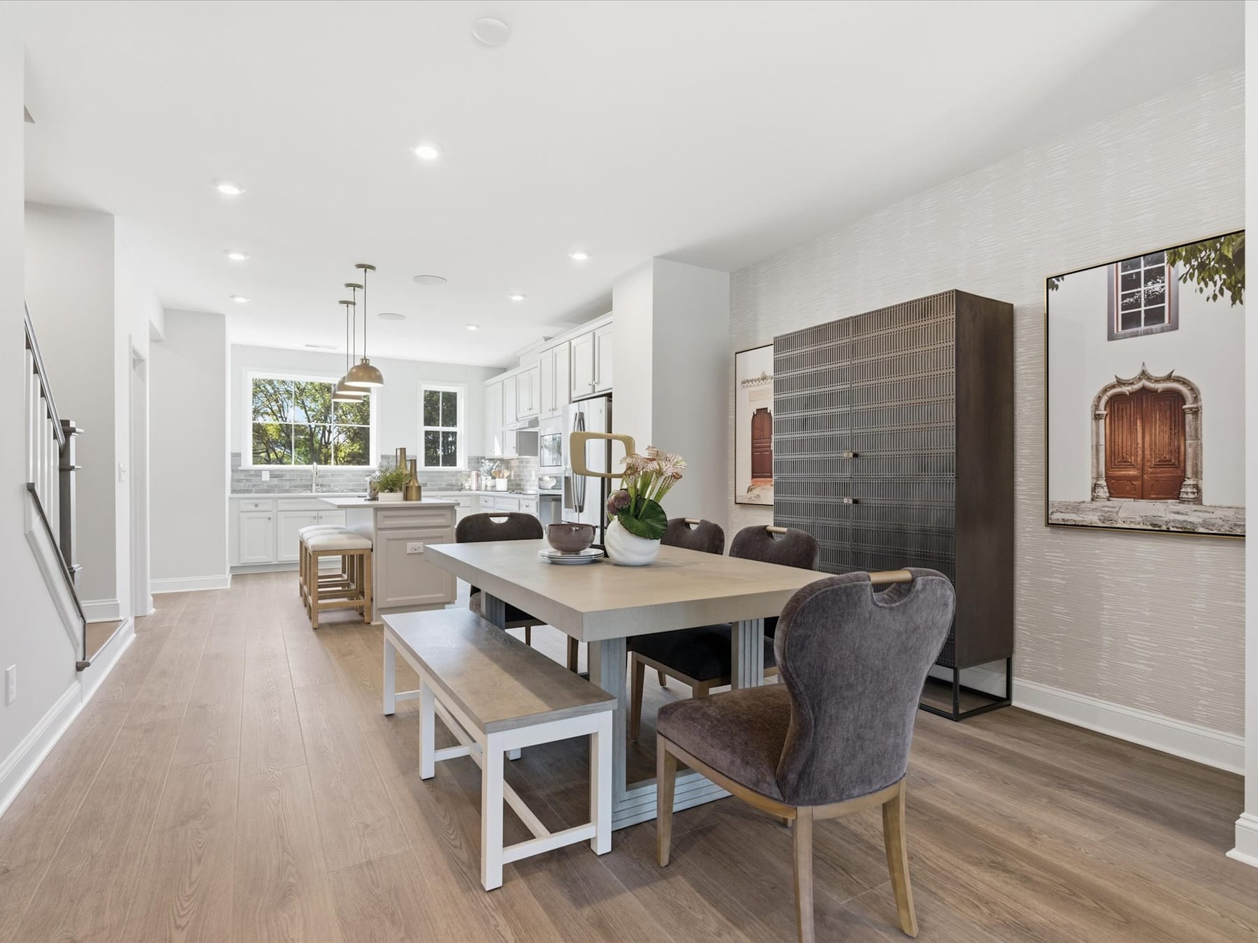 A modern and spacious open-plan kitchen and dining area with a wooden dining table, upholstered chairs, and a large window overlooking the exterior.