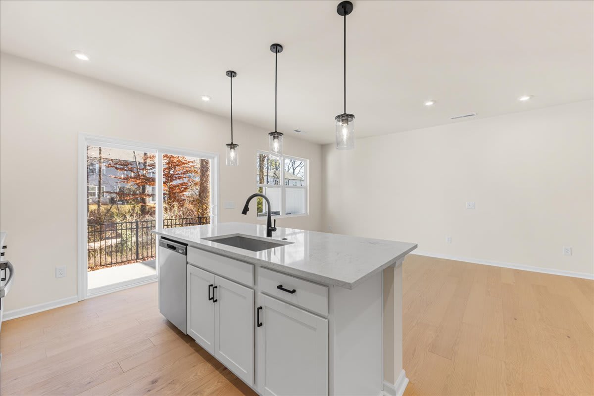 A modern kitchen with a gray island, pendant lights, and a large window overlooking a scenic outdoor view.