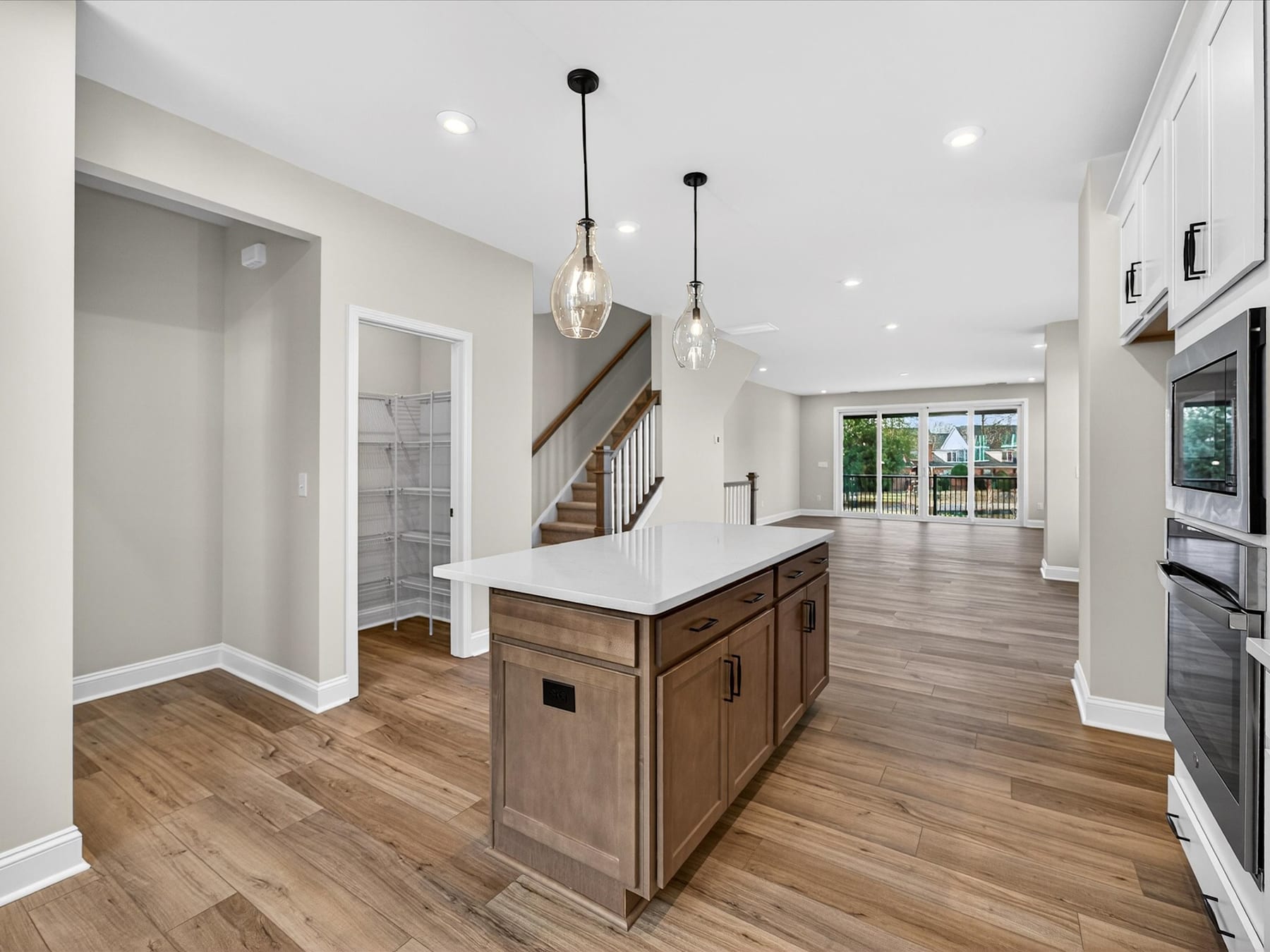 A spacious and modern kitchen with a wooden island, pendant lights, and a view of a staircase and an open living area in the background.