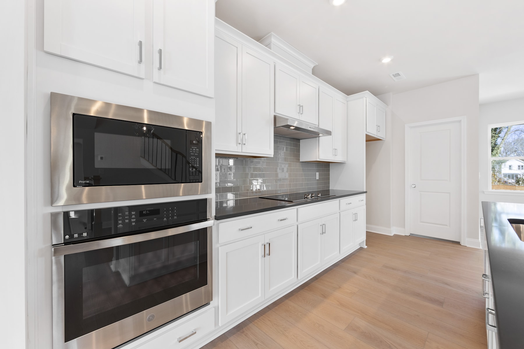 A modern, well-equipped kitchen with white cabinets, stainless steel appliances, and a tiled backsplash, set against a hardwood floor.