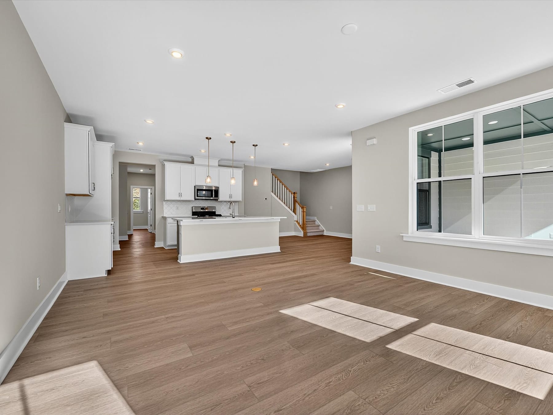 A spacious and modern open-concept kitchen and living area with white cabinets, hardwood floors, and large windows providing ample natural light.