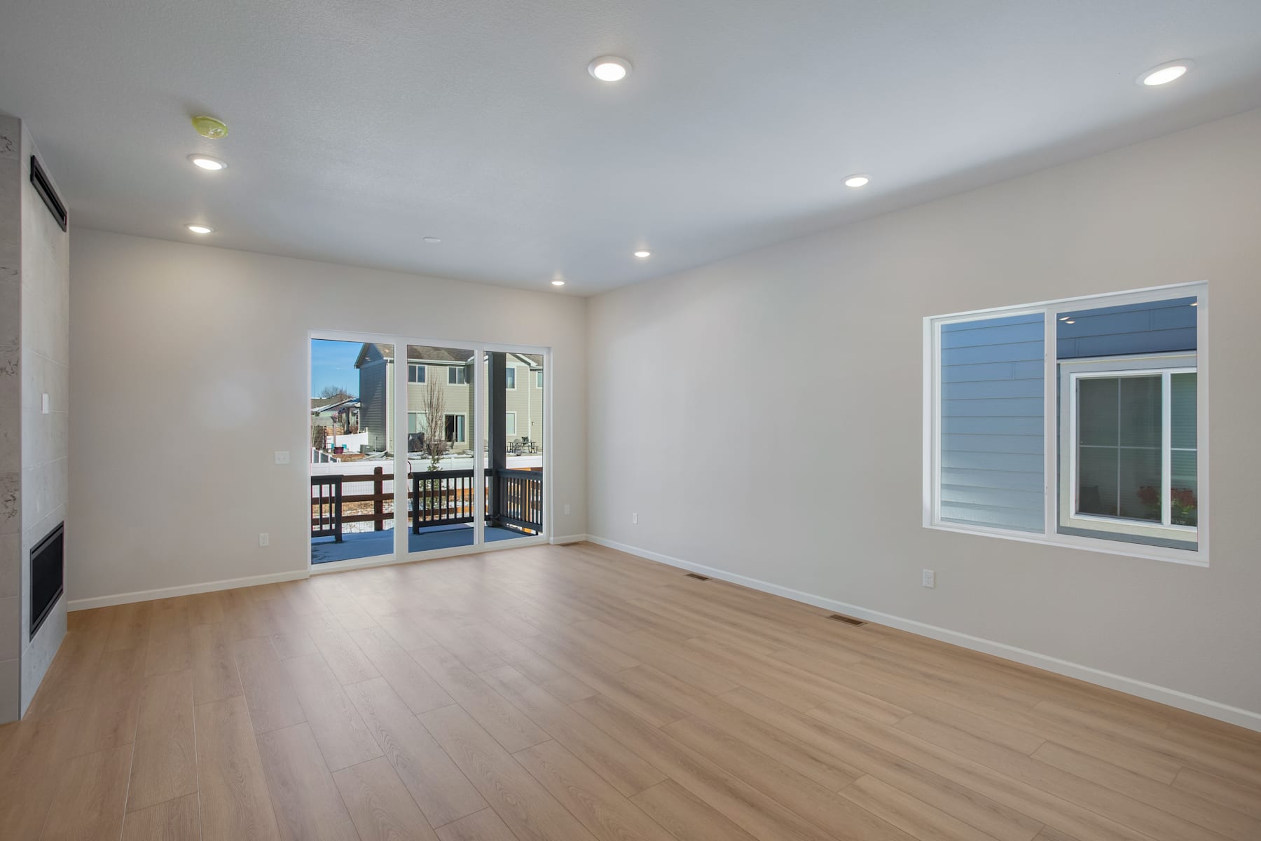 A spacious, well-lit room with a hardwood floor, recessed lighting, and a sliding glass door leading to an outdoor area.