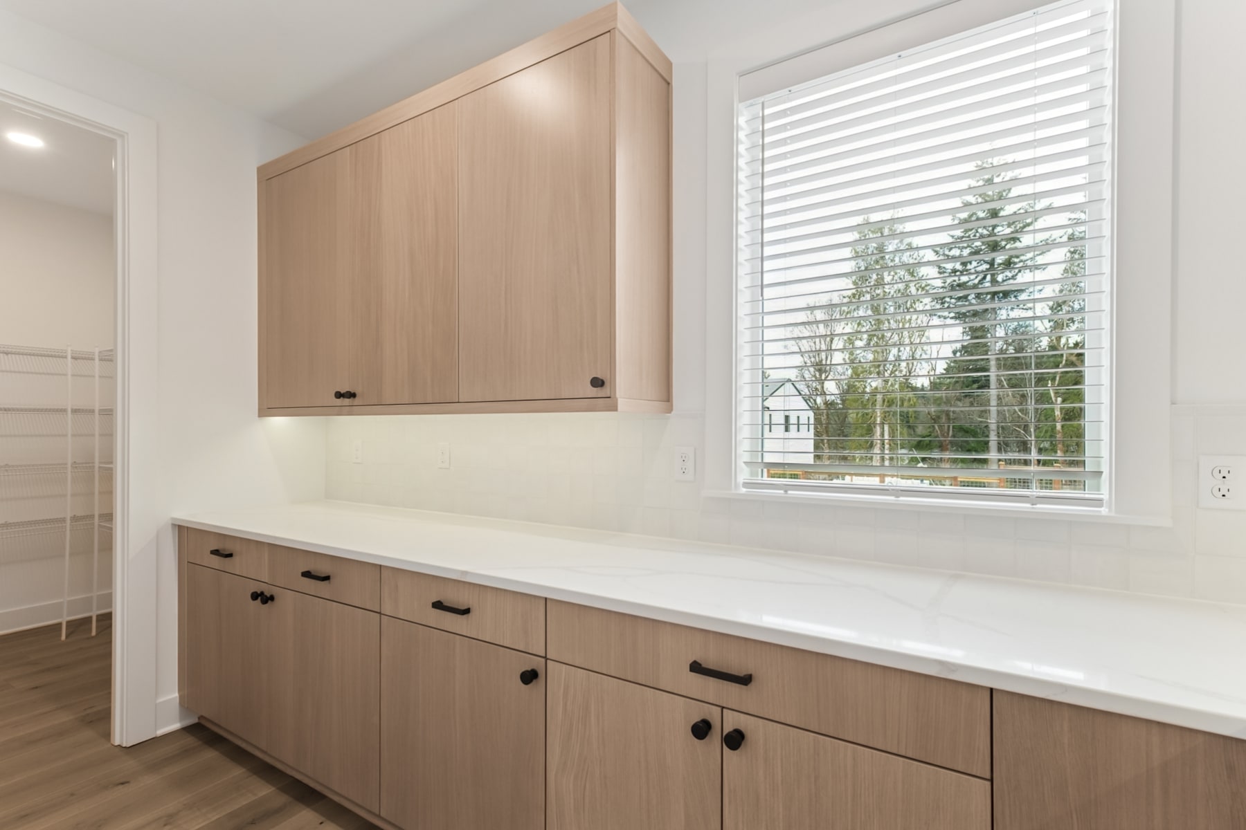 A bright and spacious laundry room with wooden cabinets, a white countertop, and a large window overlooking the outdoors.