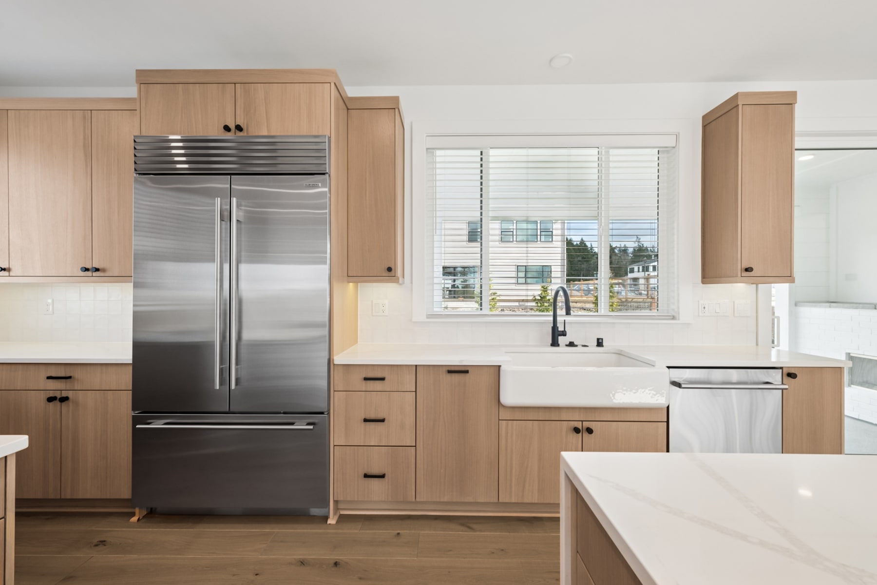 A modern, well-equipped kitchen with light wood cabinetry, stainless steel appliances, and a large window providing natural light and a view of the outdoors.