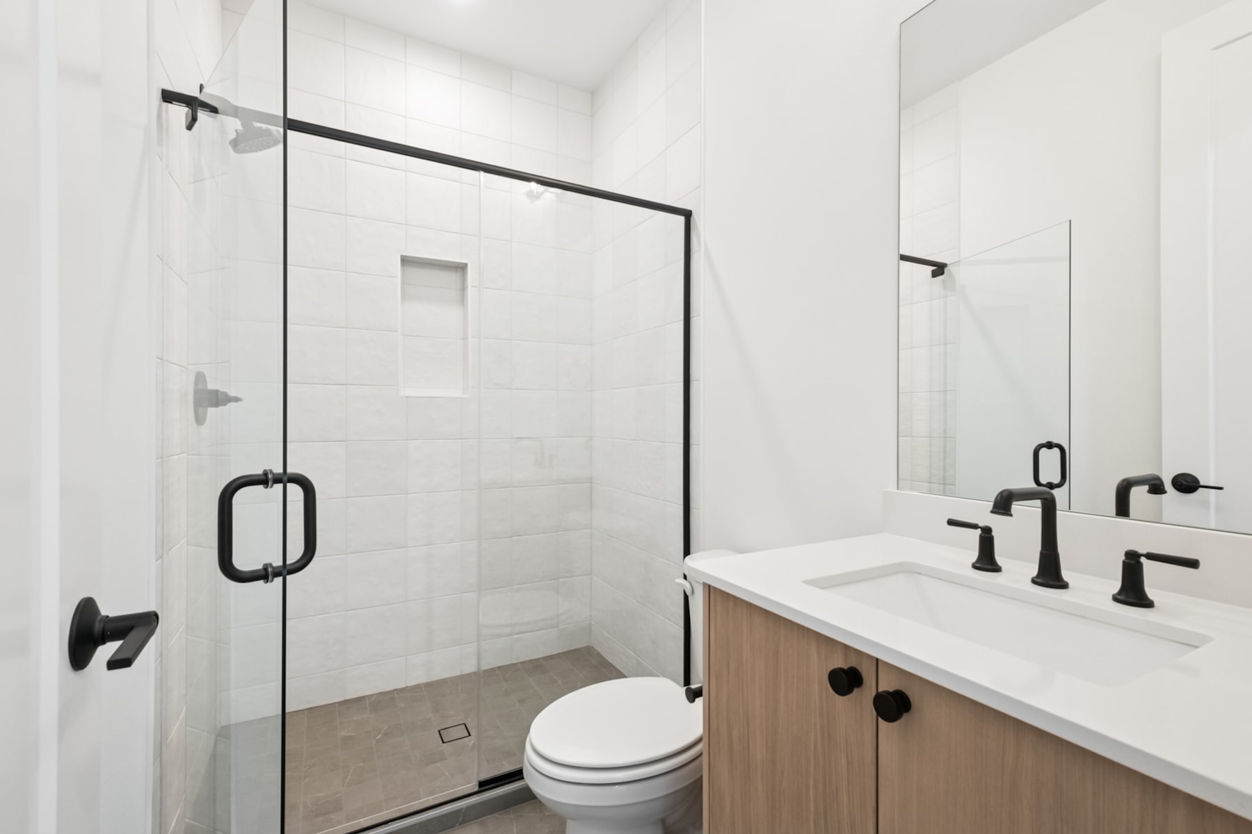 A modern, minimalist bathroom with a glass shower enclosure, a wooden vanity, and a white toilet.