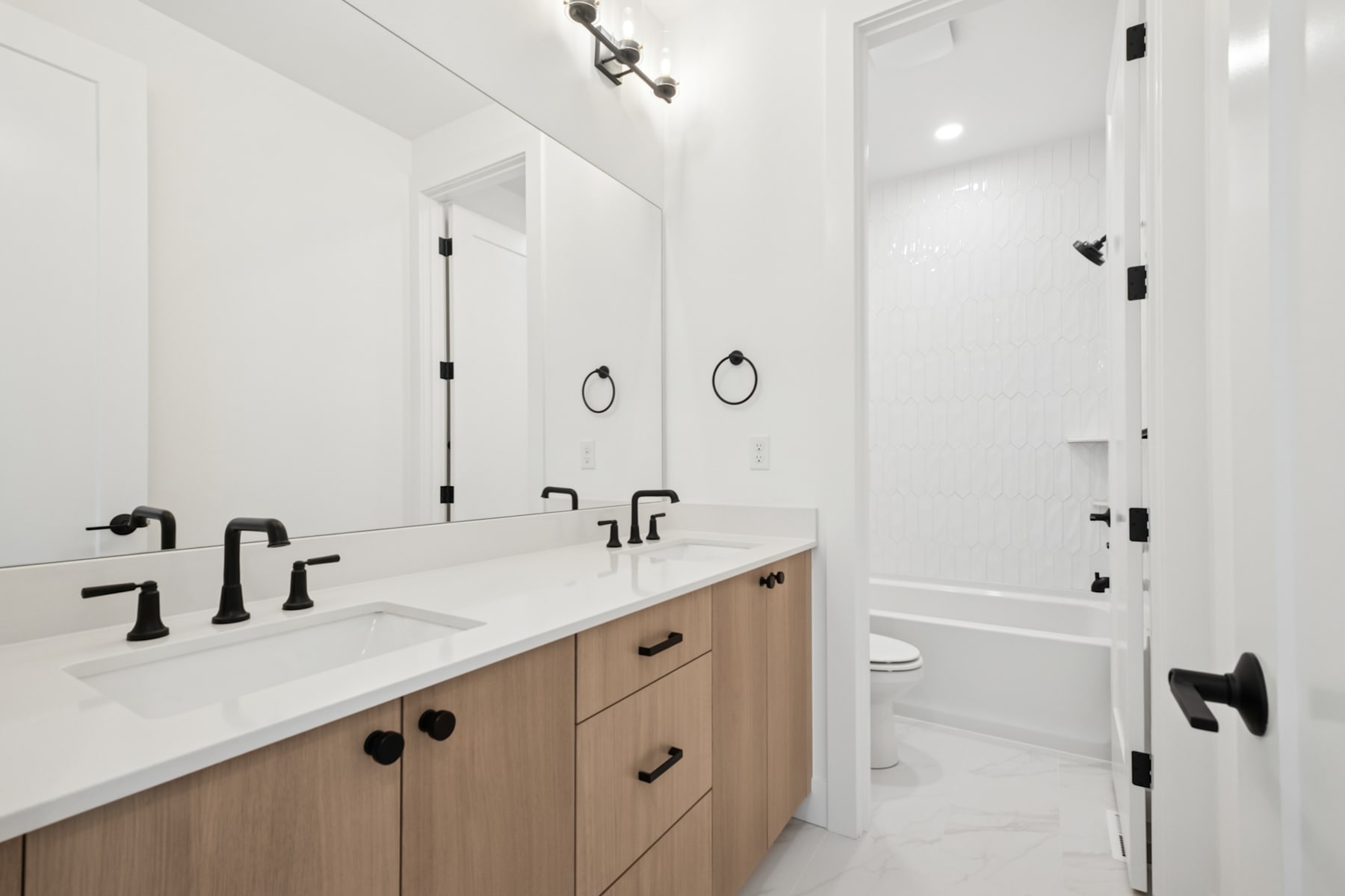 A modern, minimalist bathroom with a double vanity, white countertops, and black fixtures, set against a bright, airy backdrop.