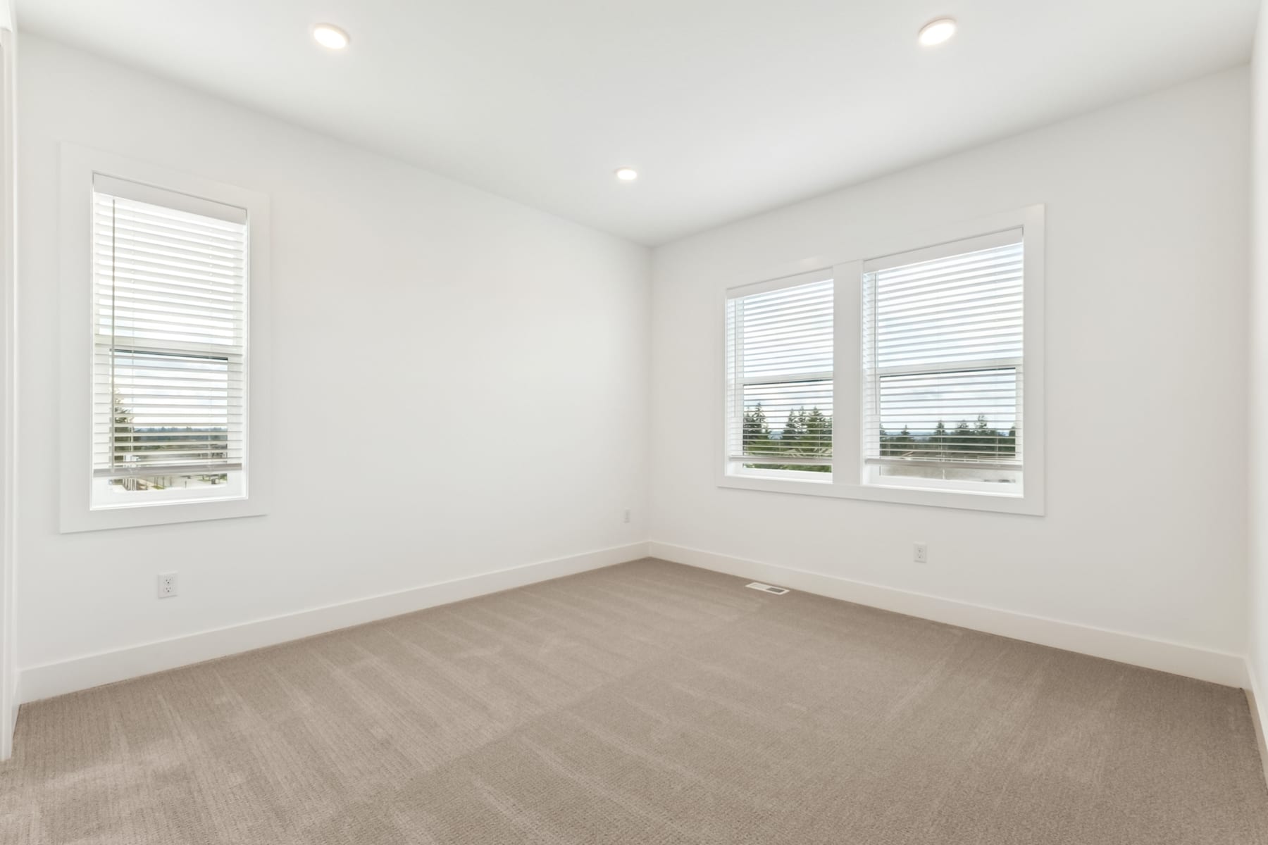 A bright, empty room with white walls, large windows, and a hardwood floor.