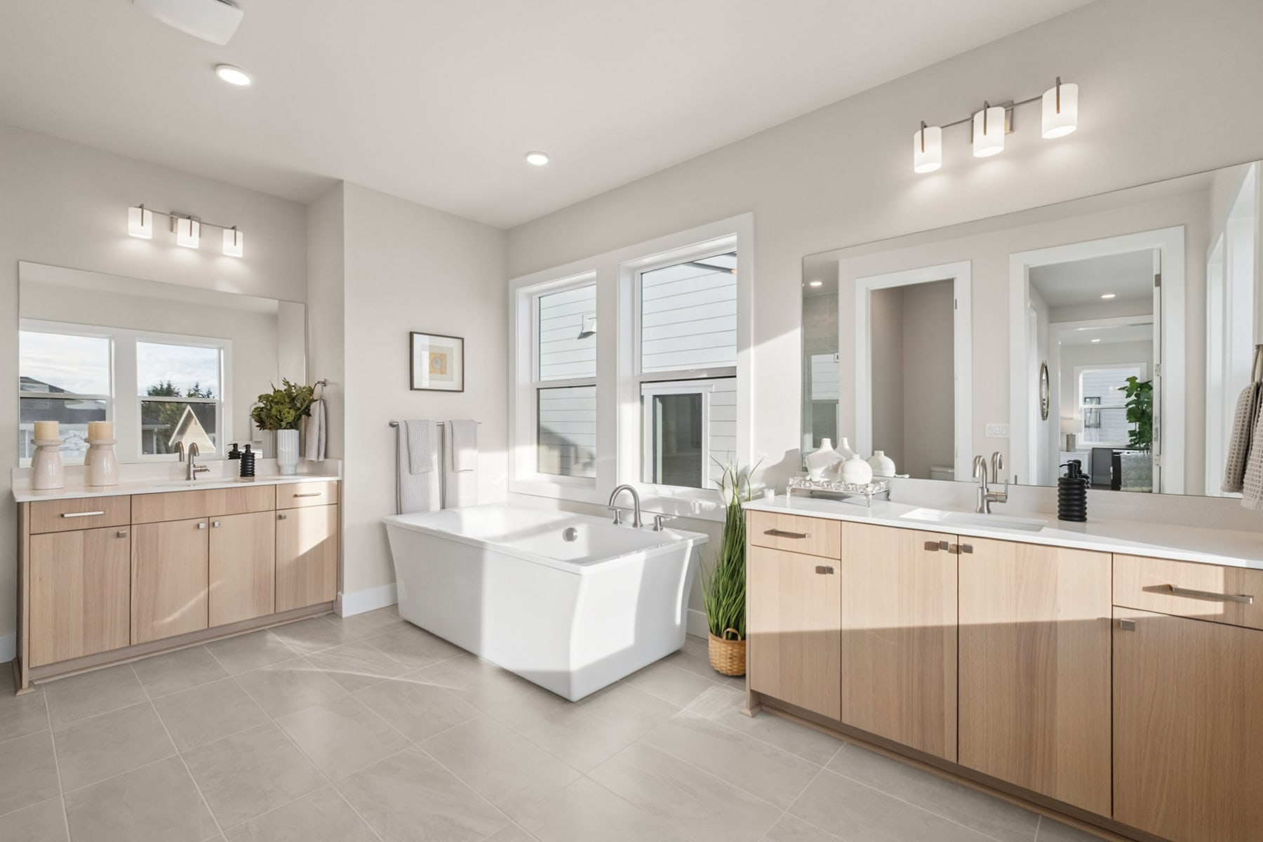 A spacious and modern bathroom with a white bathtub, wooden cabinets, and large windows allowing natural light to fill the room.