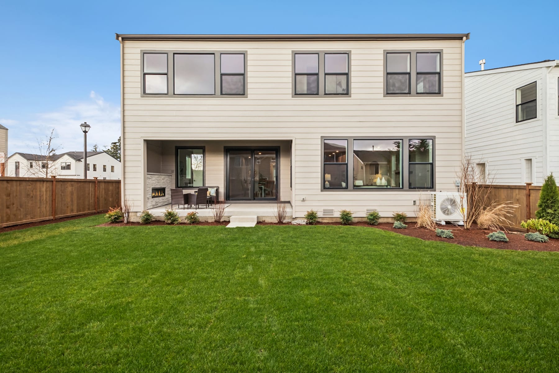 A well-manicured lawn and a modern, two-story wooden house with large windows and a porch in a residential neighborhood.